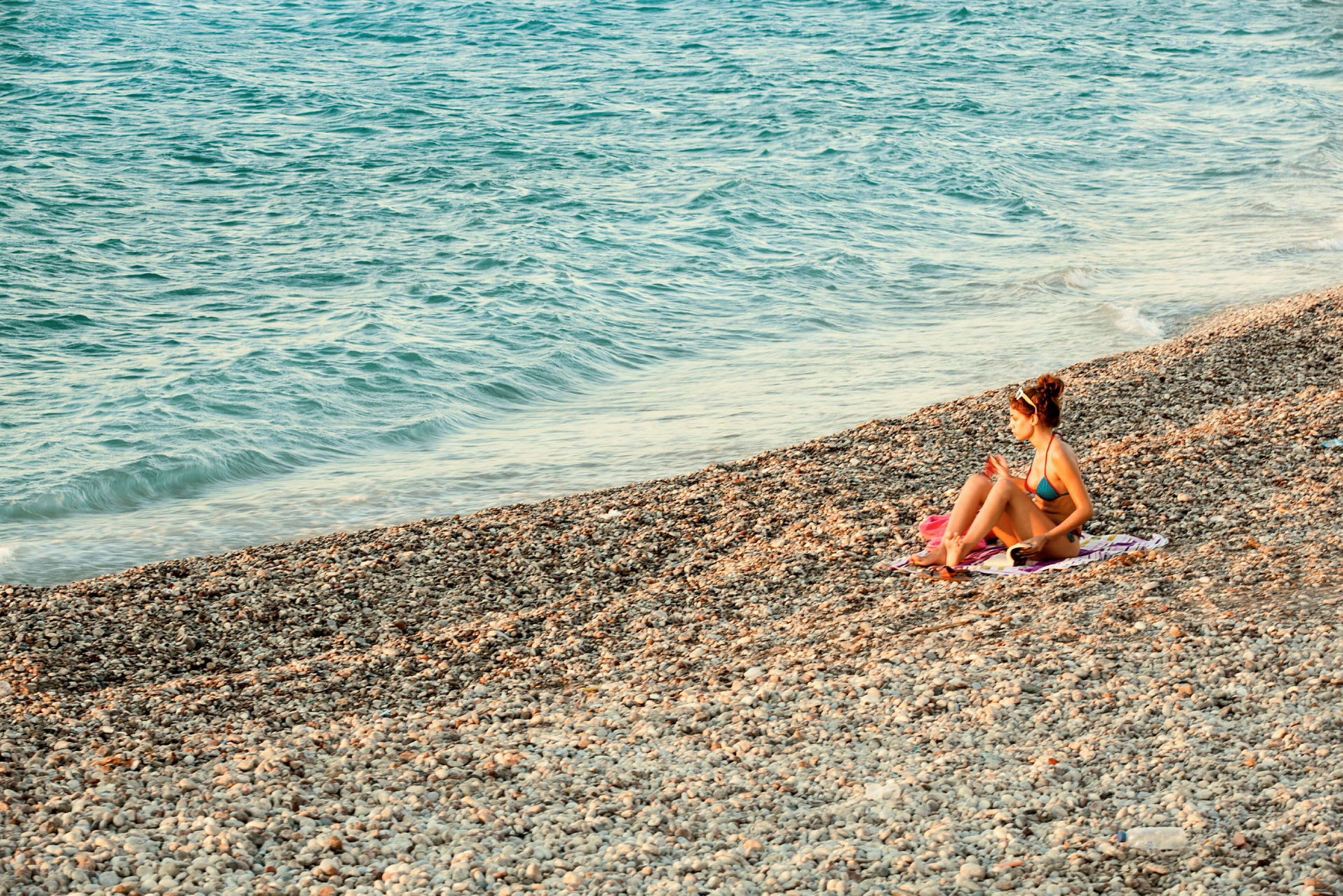 Person sitter på en steinete strand nær havet. (AI-generert tekst)