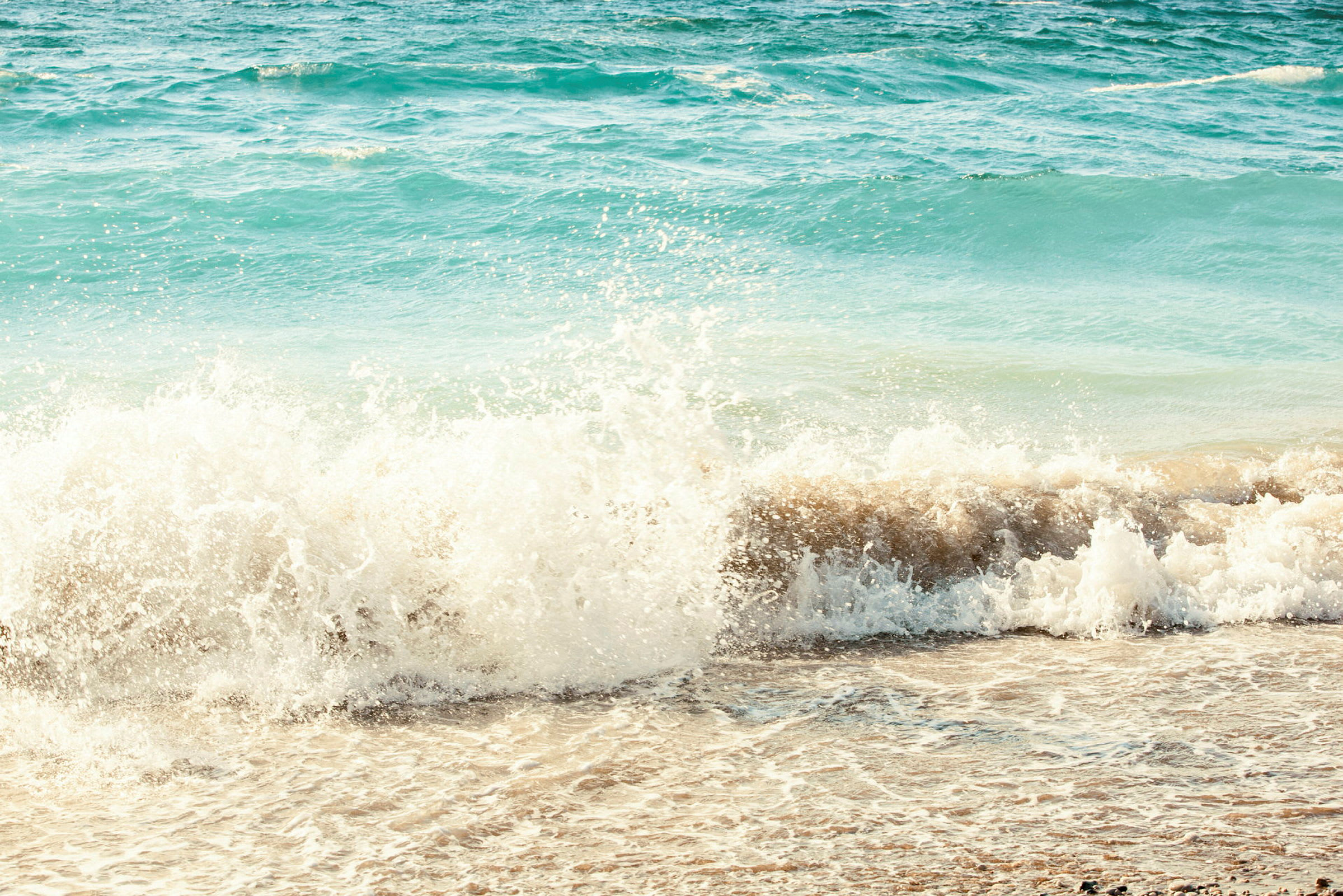 En bølge bryter mot en sandstrand ved havet. (AI-generert tekst)