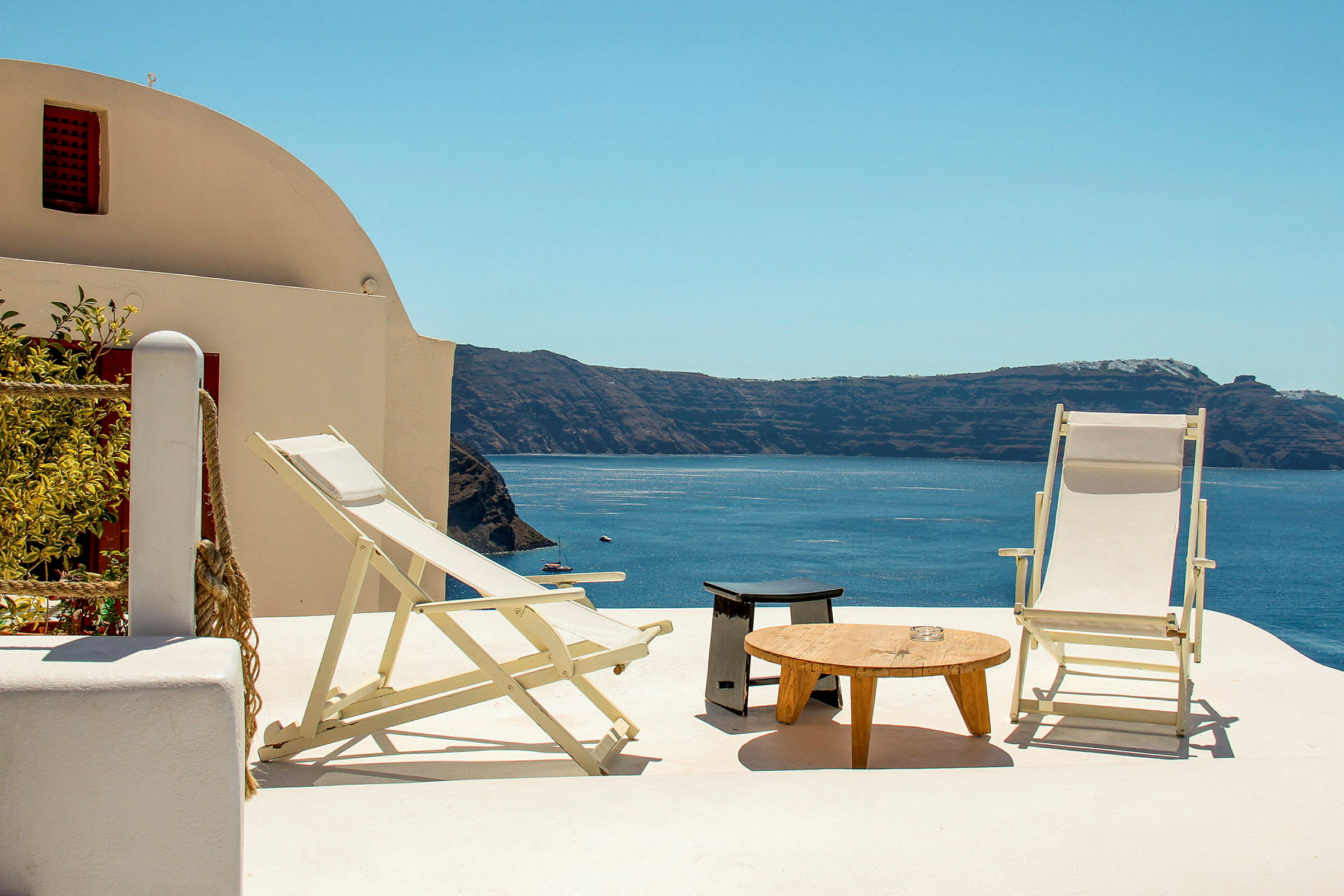 To solsenger og et bord på en terrasse med utsikt over havet og klipper. (AI-generert tekst)