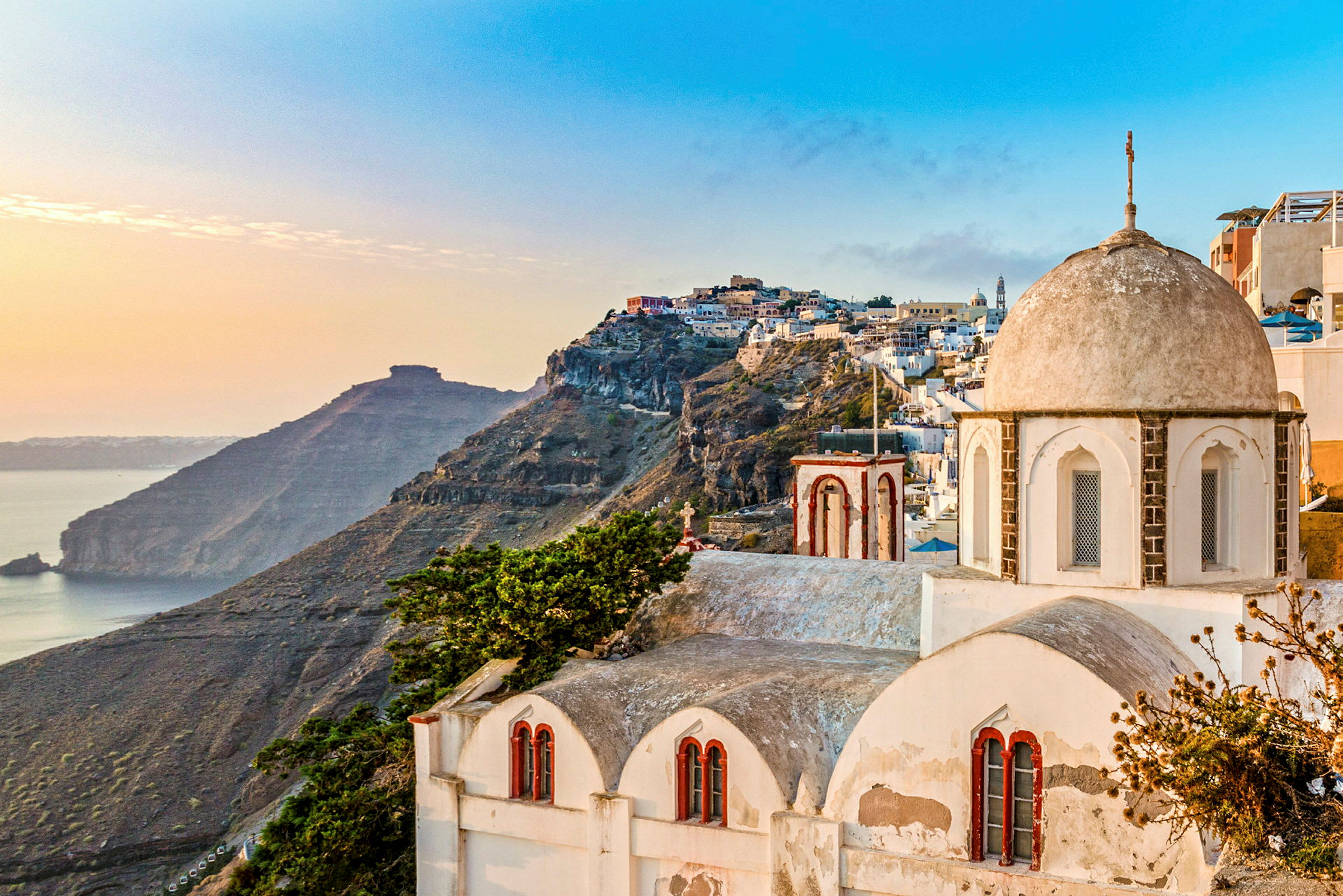 Utsikt over Santorini med sine karakteristiske hvite bygninger og en klippe ved havet i solnedgangen. (AI-generert tekst)