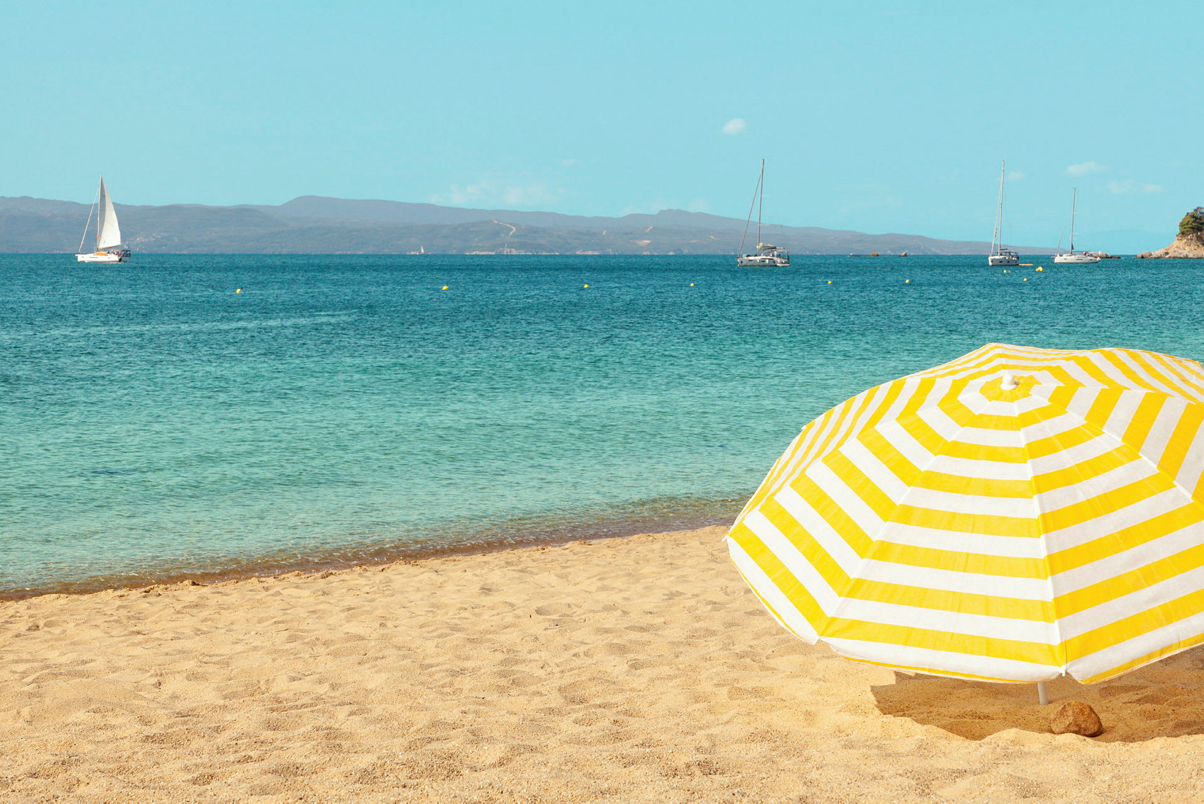 Gulstripete parasoll på en sandstrand med havet i bakgrunnen. (AI-generert tekst)