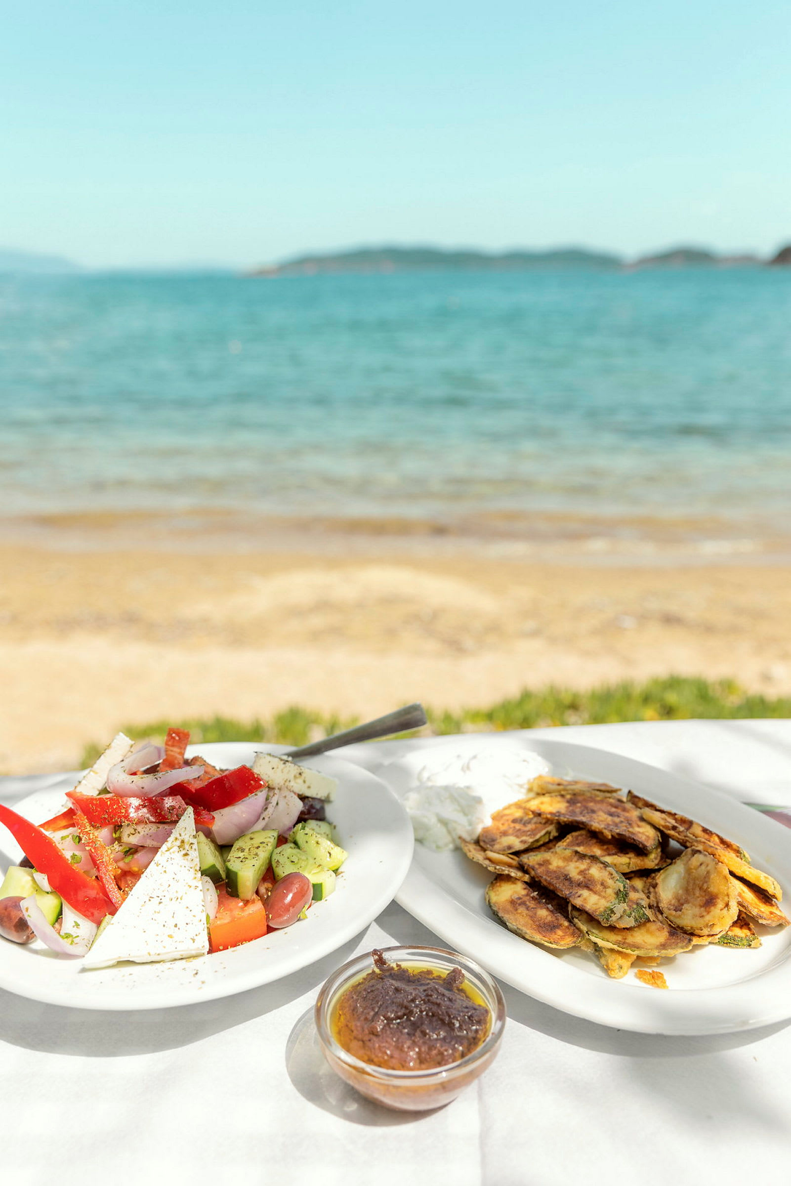 To tallerkener med mat og en skål med saus, servert med utsikt over stranden og havet. (AI-generert tekst)