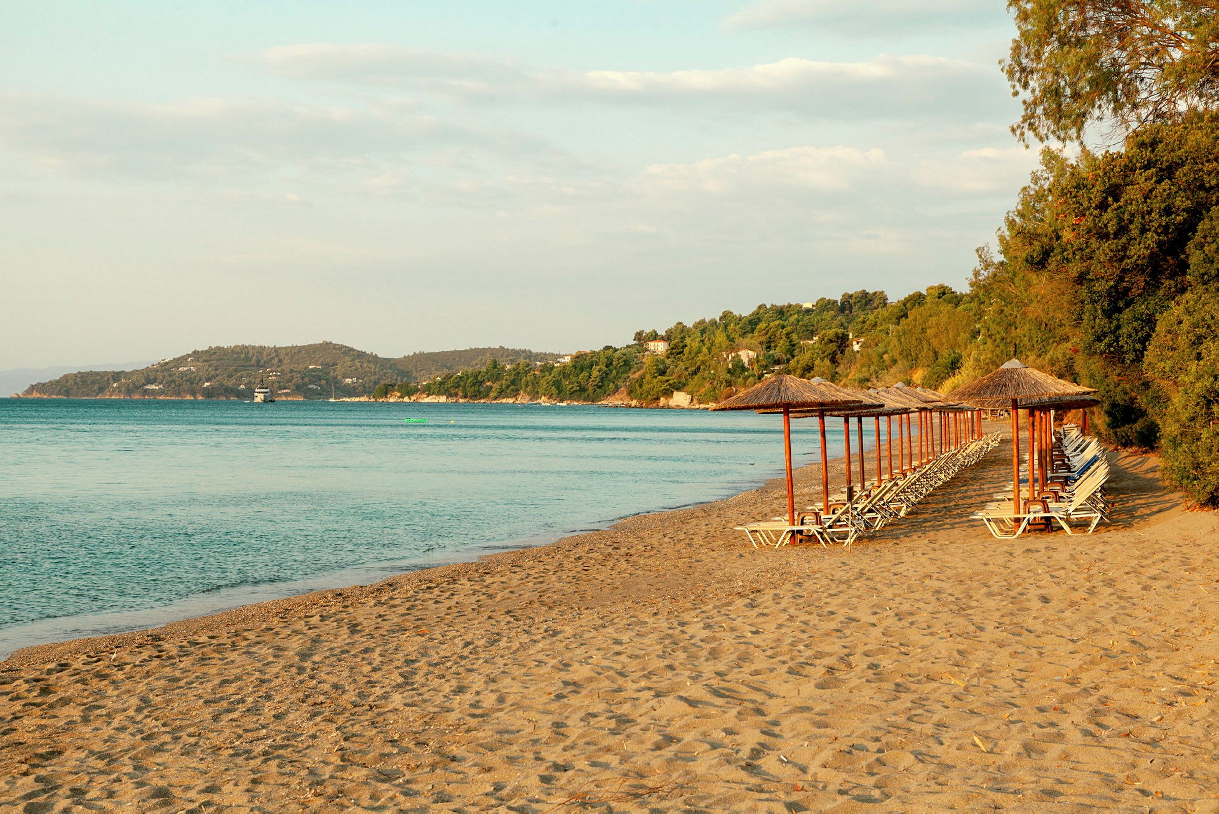 Strand med parasoller og solsenger ved havet. (AI-generert tekst)