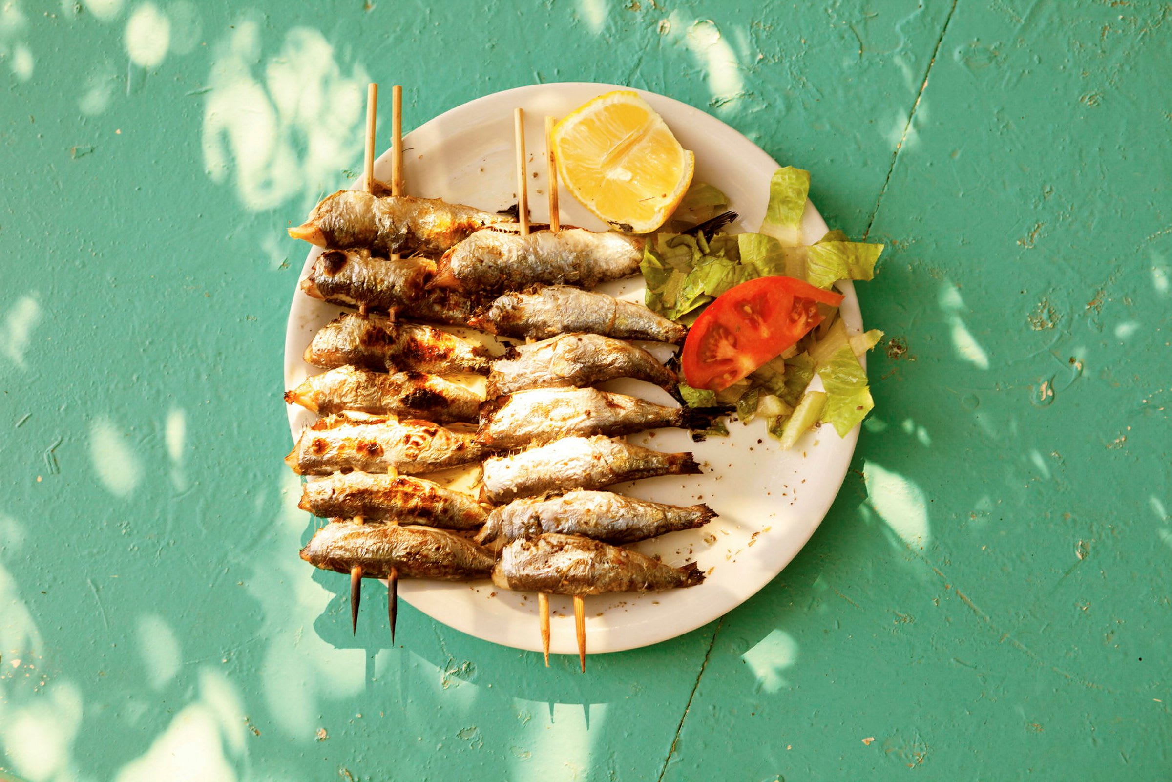 En tallerken med grillede fisker på spyd, servert med salat, tomat og en sitronskive. (AI-generert tekst)