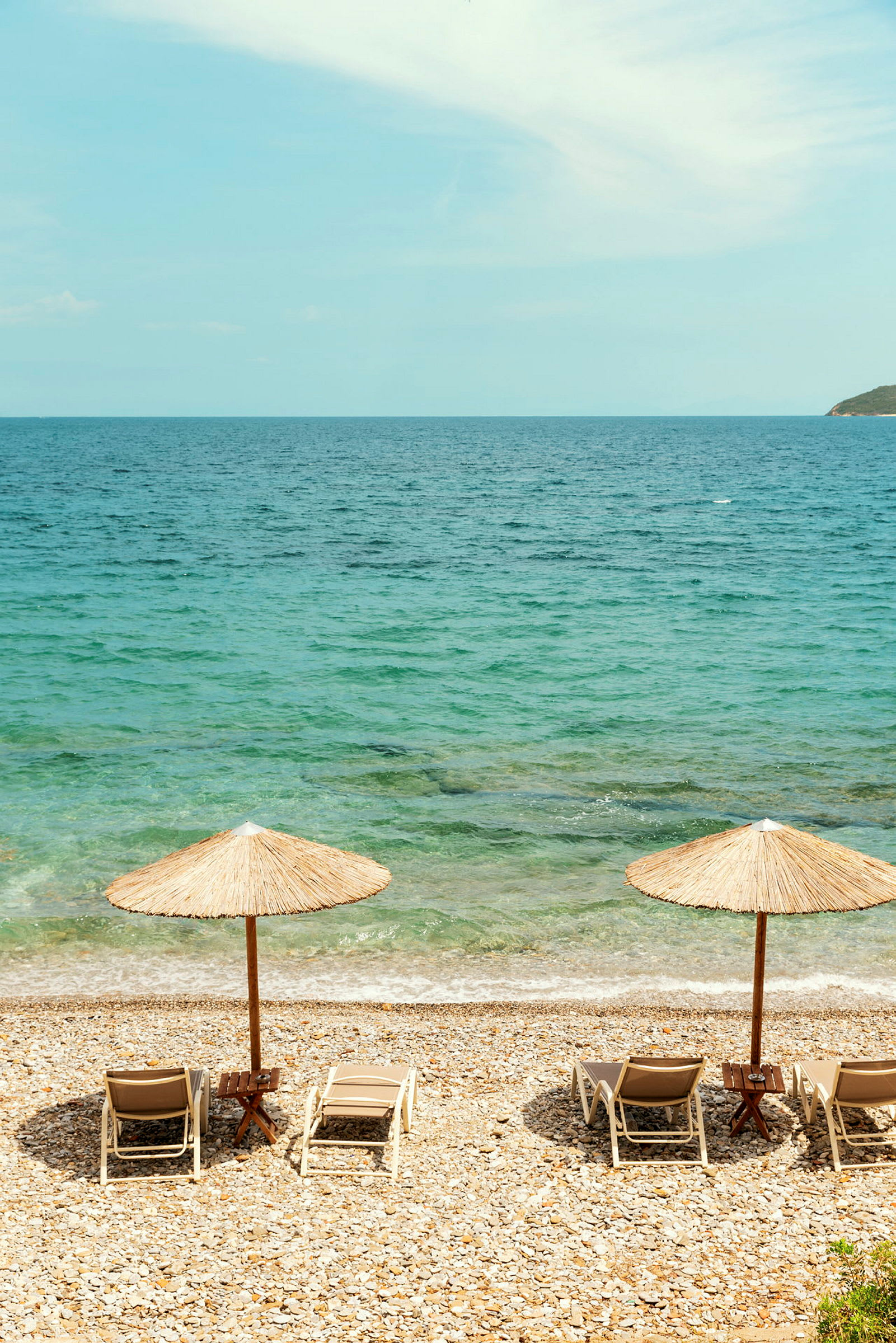 To solsenger med parasoller på en steinete strand ved havet. (AI-generert tekst)