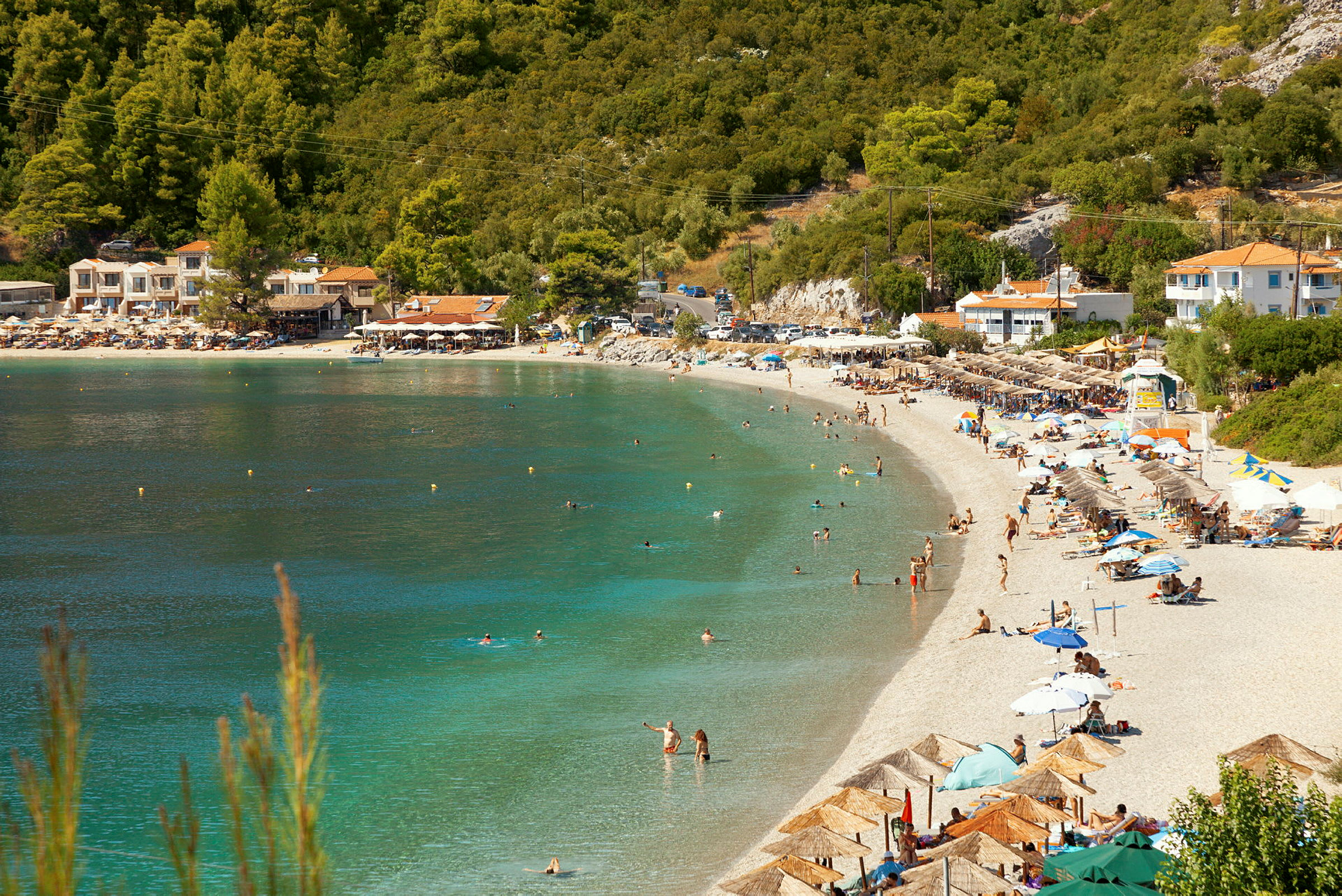 Strand med turkis vann, besøkende og parasoller med en frodig bakgrunn. (AI-generert tekst)