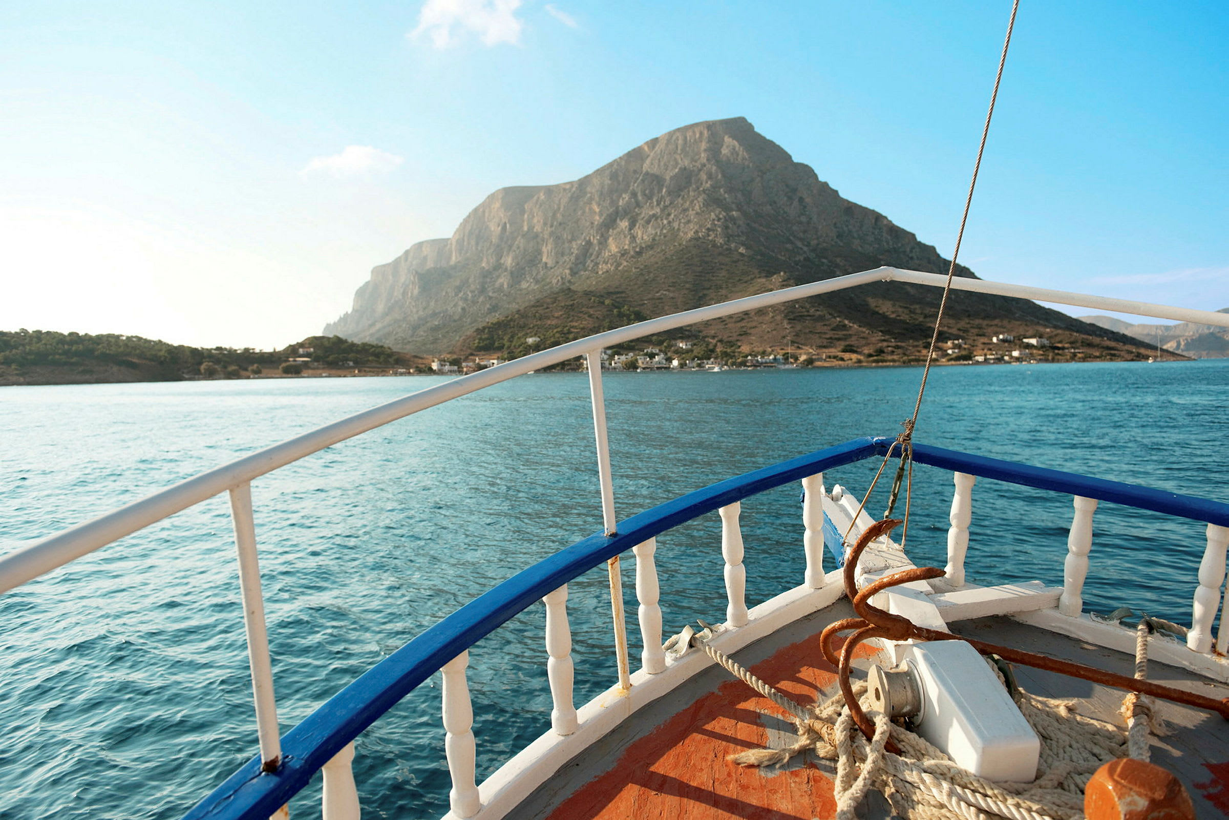 Bådens fordekk med rekkverket i forgrunnen, med vann og en bergøy i bakgrunnen. (AI-generert tekst)