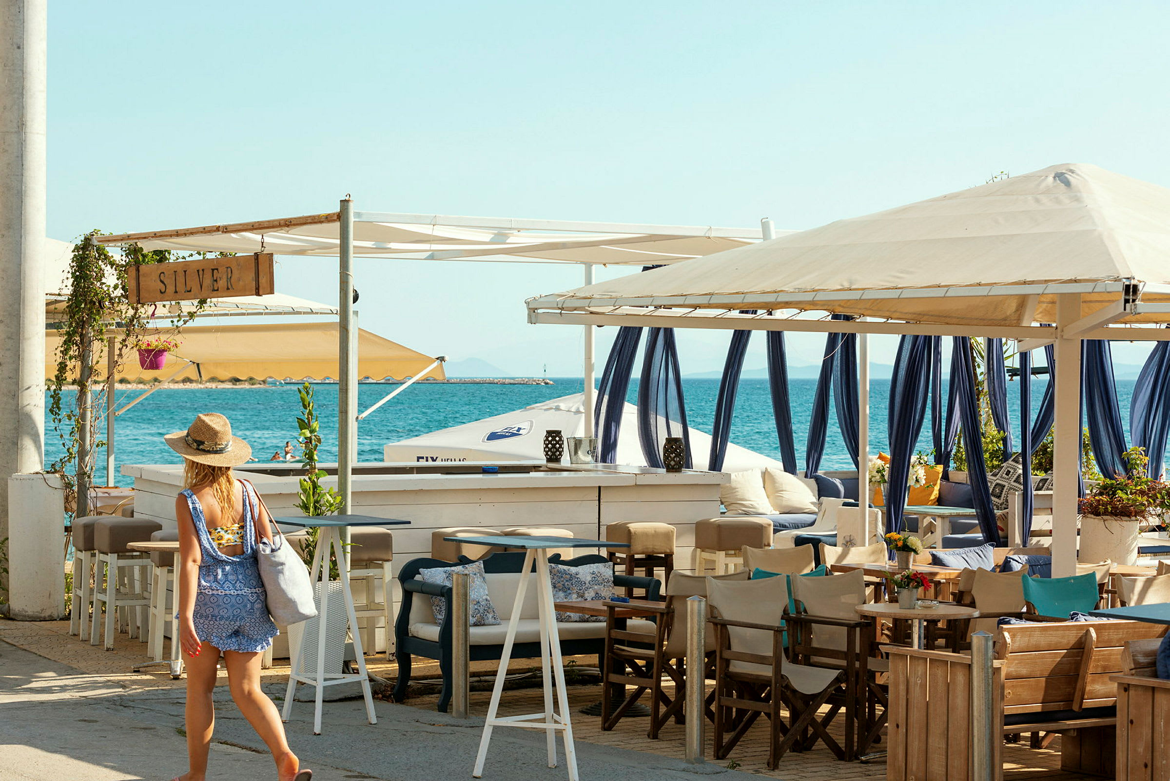 Bilde av en person som går ved en strandbar med sitteplasser og hav i bakgrunnen. (AI-generert tekst)
