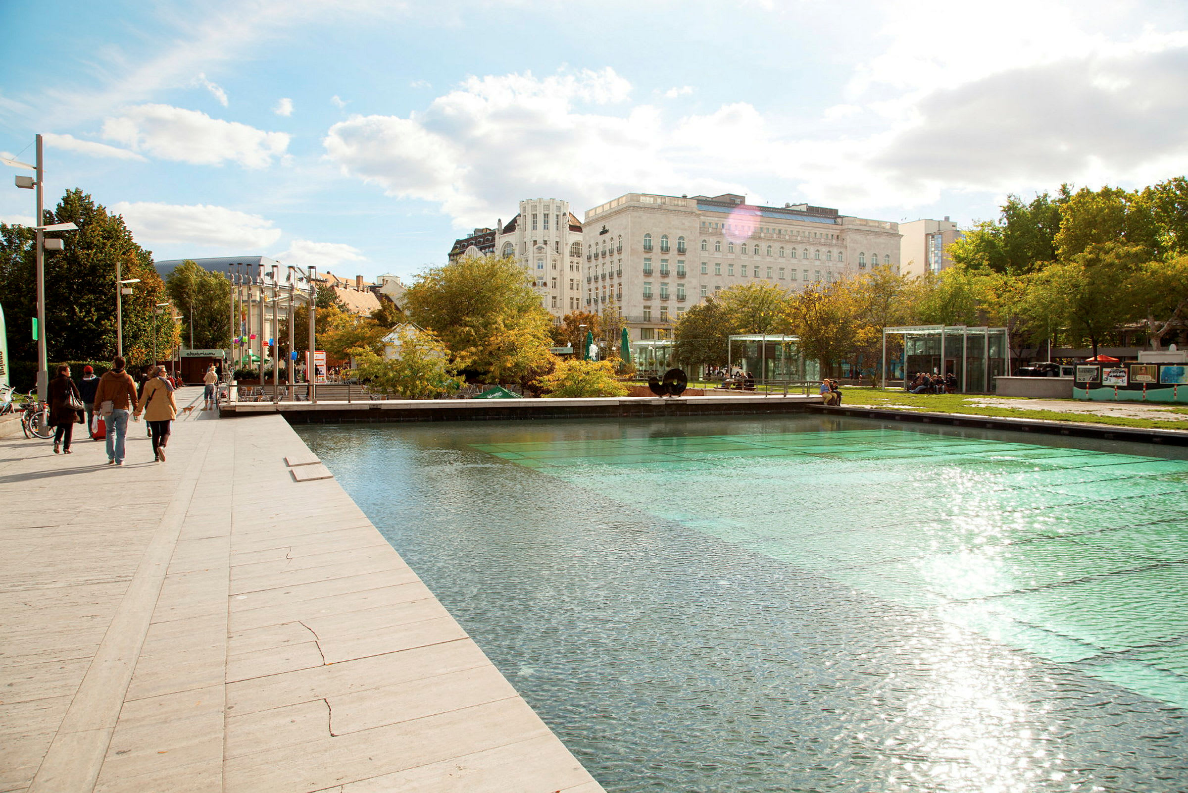 En gangvei ved en moderne park med en reflekterende vannoverflate og grøntområder. (AI-generert tekst)