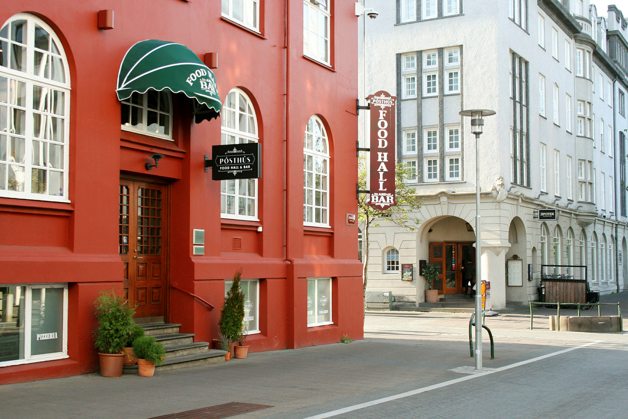 Et rødt hus med store vinduer og en grønn markise hvor det står "Food Hall & Bar". (AI-generert tekst)