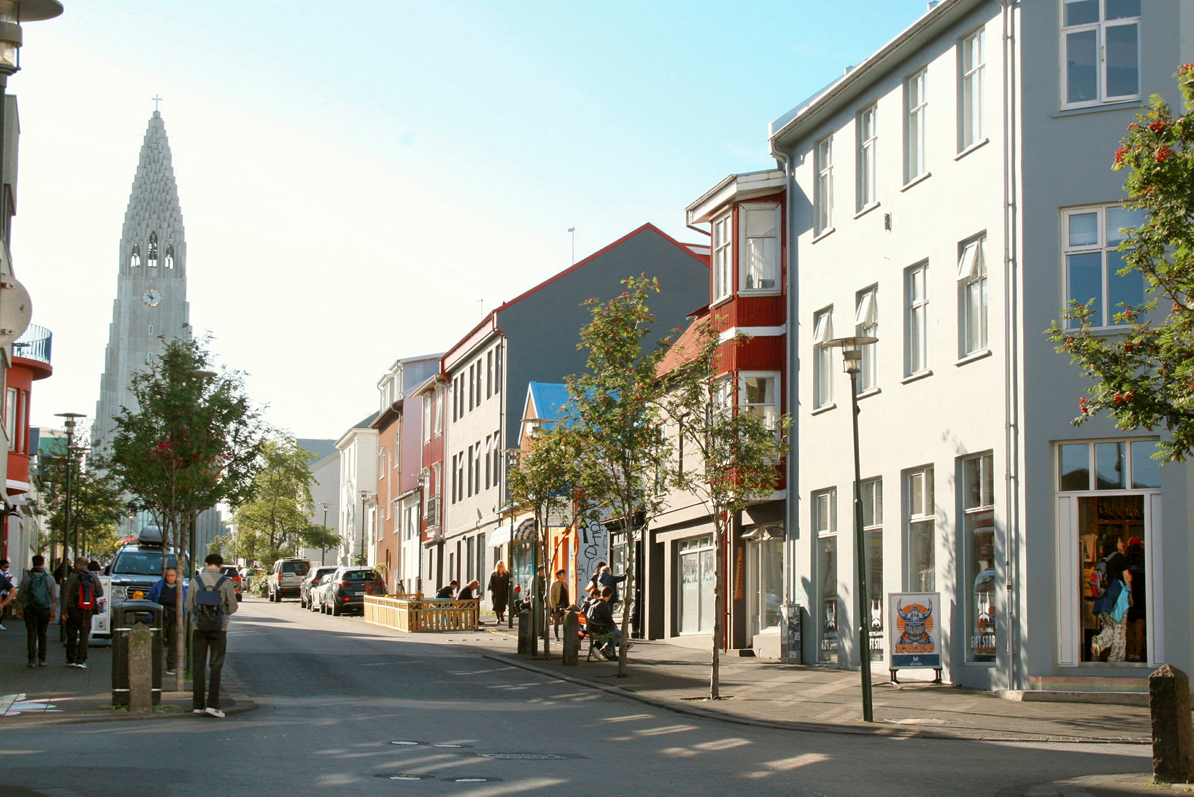 En gate med mennesker, bygninger og en kirke med spir i bakgrunnen. (AI-generert tekst)