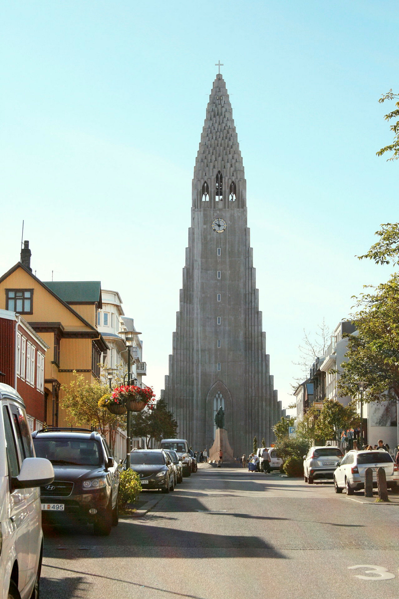 Et bilde av en gate med biler parkert på sidene, og i bakgrunnen sees en høy kirke med unik arkitektur. (AI-generert tekst)