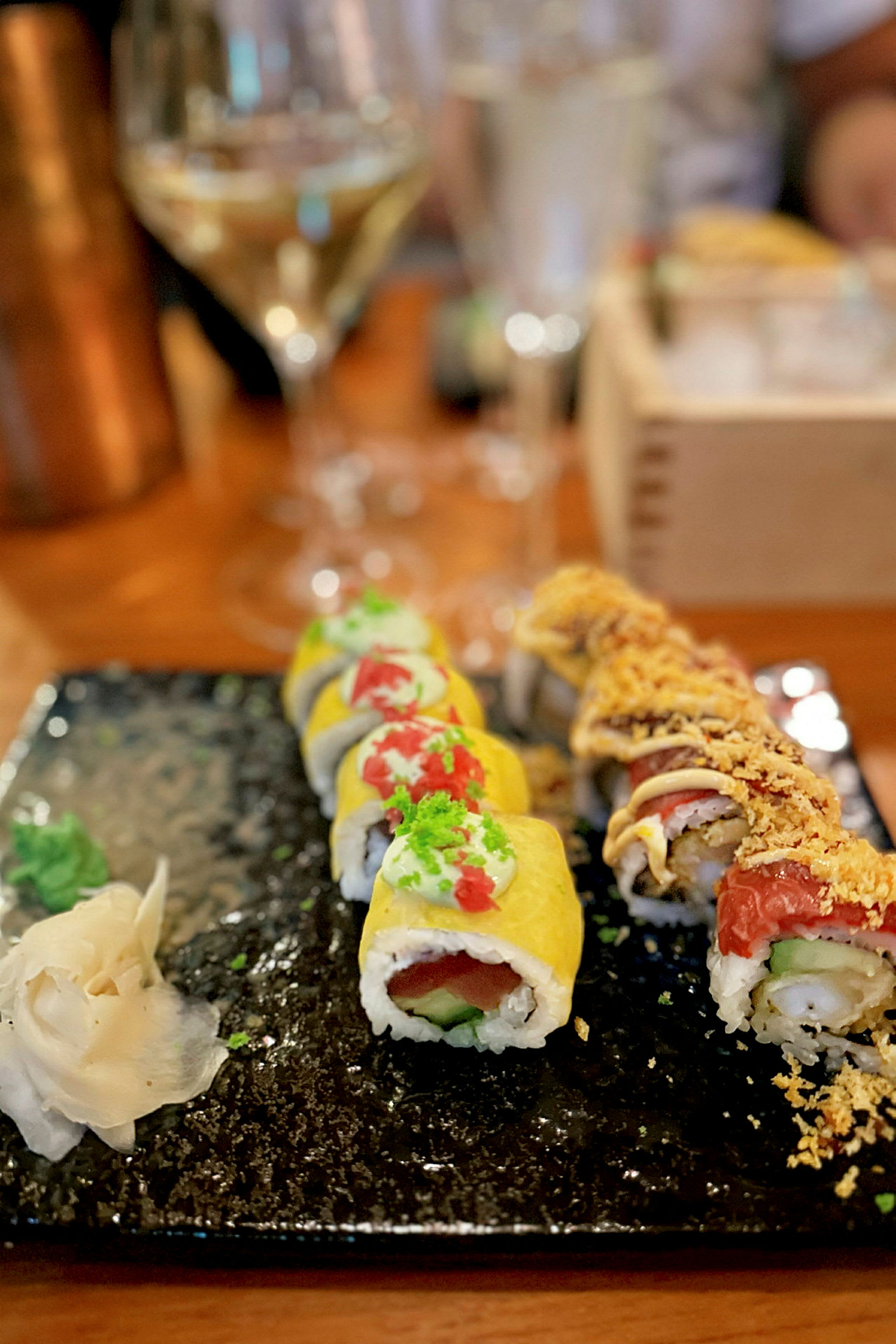 En tallerken med to rekker sushi og tilbehør, servert på et mørkt fat. (AI-generert tekst)