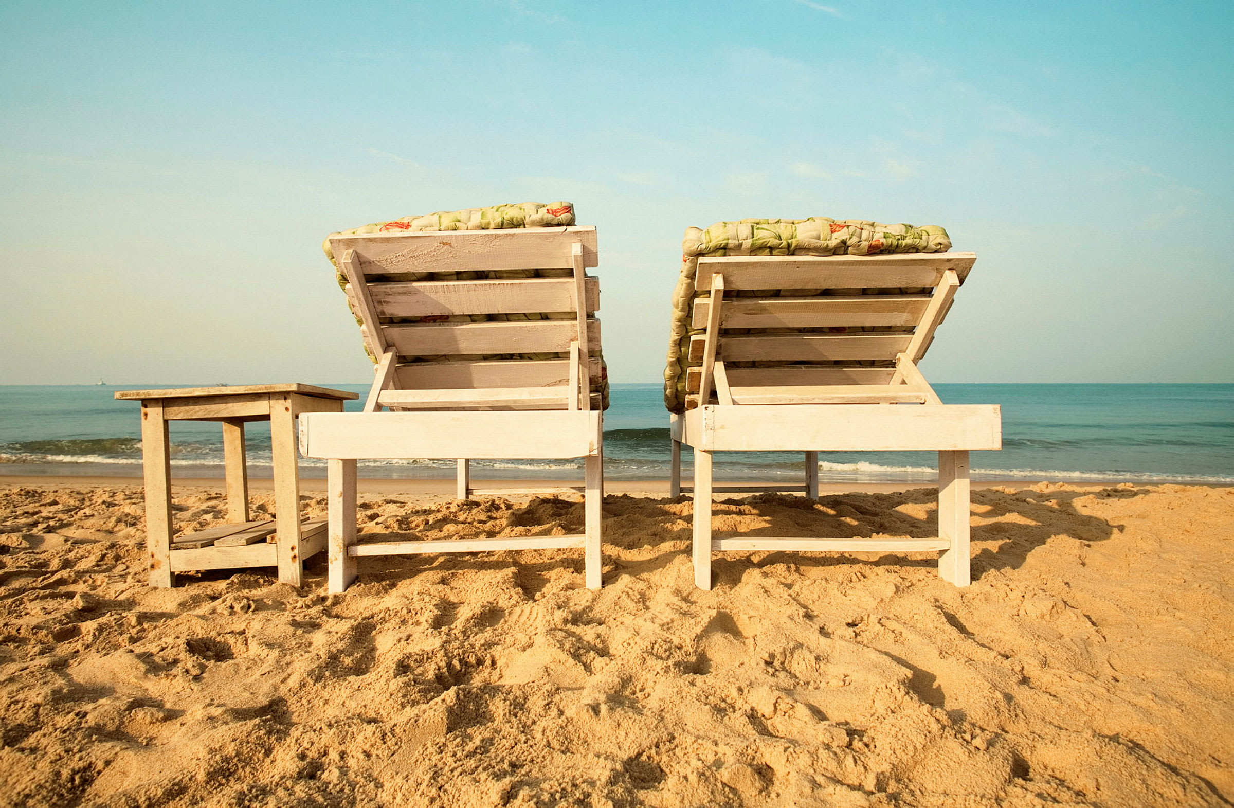 Bilde av to solsenger og et lite bord på en sandstrand ved havet. (AI-generert tekst)