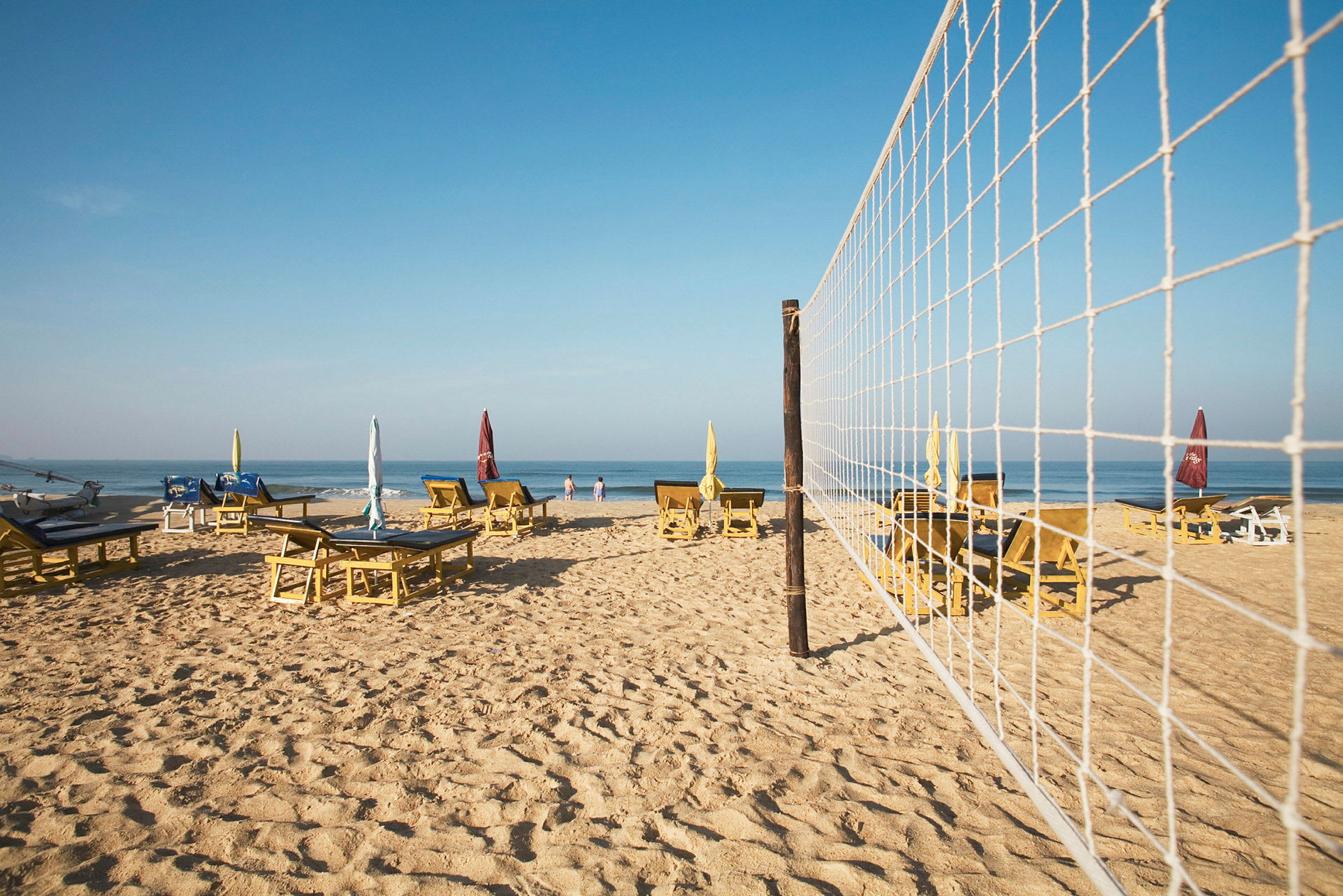 Strand med solsenger, parasoller og et volleyballnett. (AI-generert tekst)