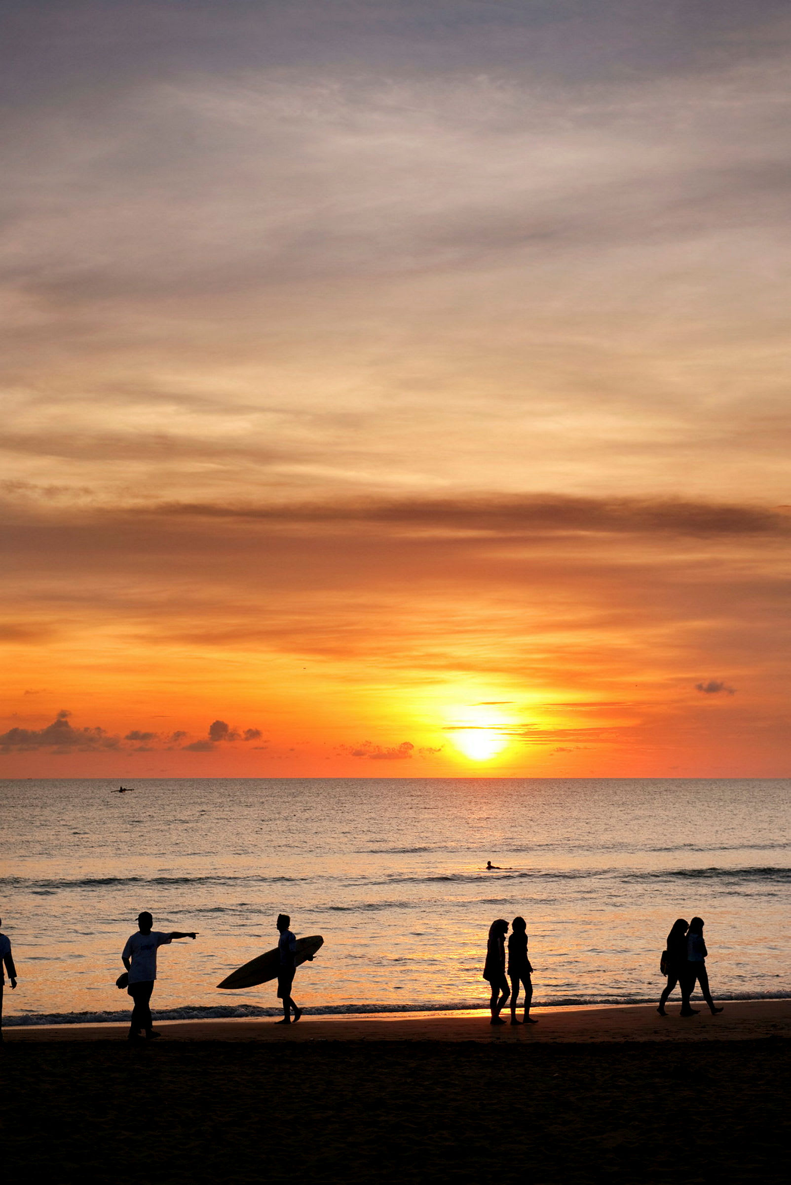Solnedgang over havet med silhuetter av mennesker på stranden. (AI-generert tekst)