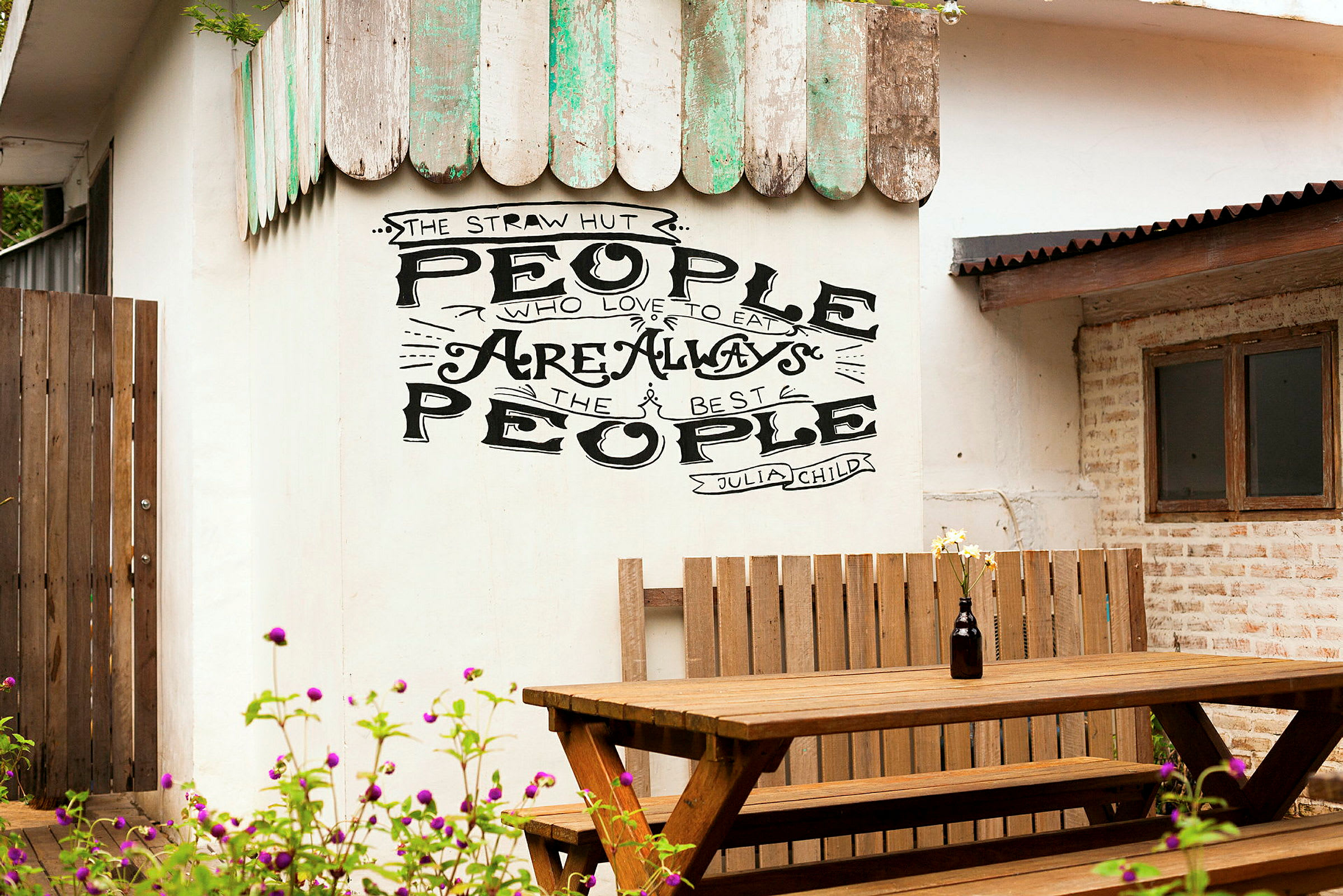 Veggen med teksten 'People who love to eat are always the best people' over en trebenk og et bord. (AI-generert tekst)