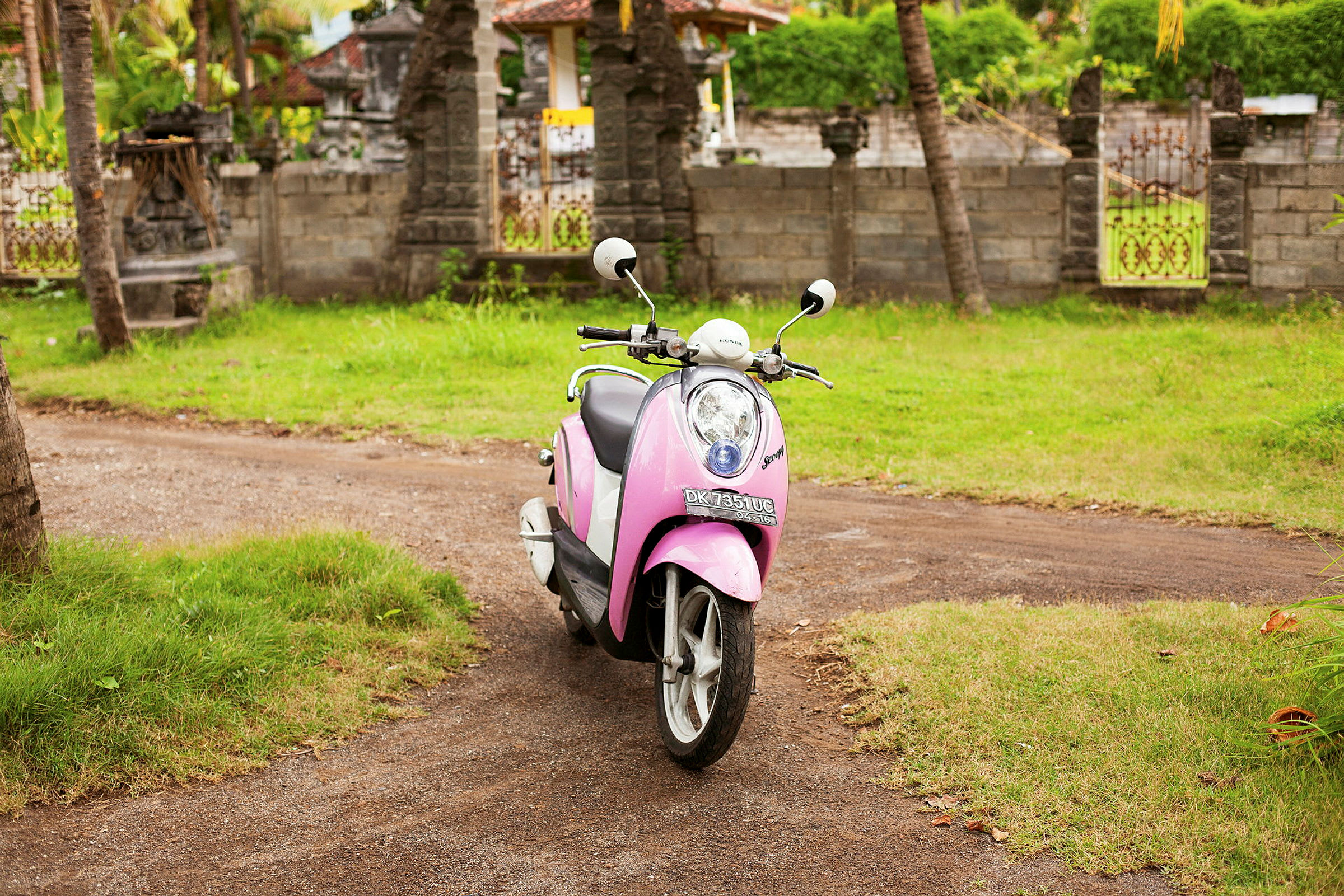 En rosa scooter står parkert utendørs på en grusvei. (AI-generert tekst)
