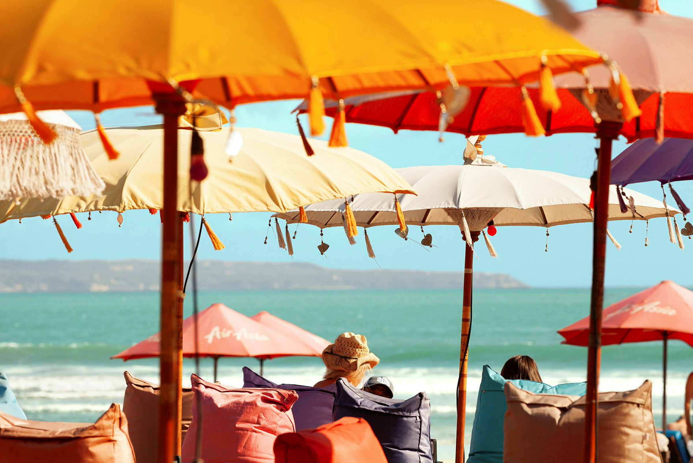 Fargerike parasoller på en strand med personer som sitter under dem. (AI-generert tekst)