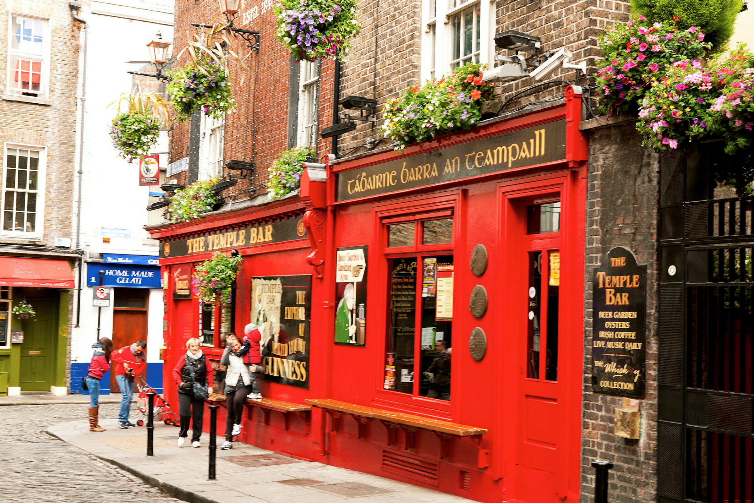 En rød bygning med skiltet 'The Temple Bar' med blomsterkasser og folk utenfor. (AI-generert tekst)