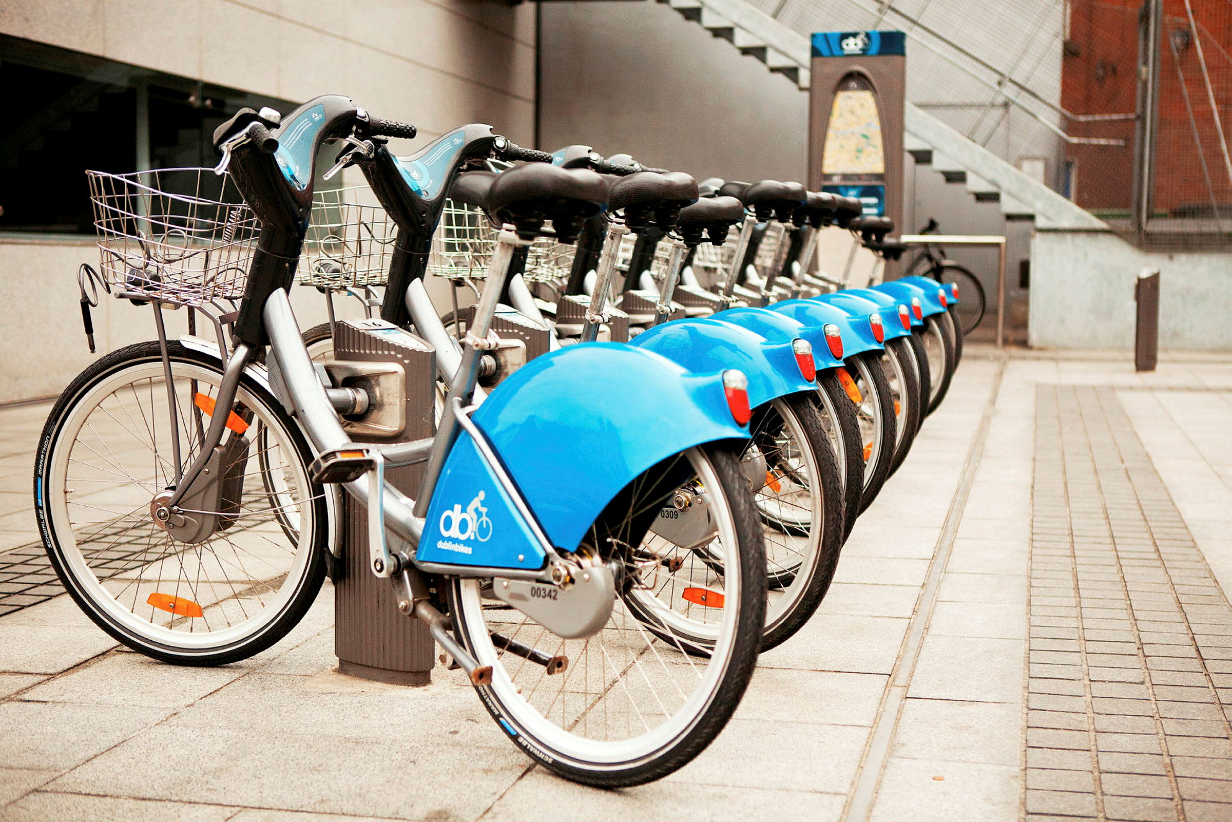 En rekke parkerte blå leiesykler på rad ved en stasjon. (AI-generert tekst)