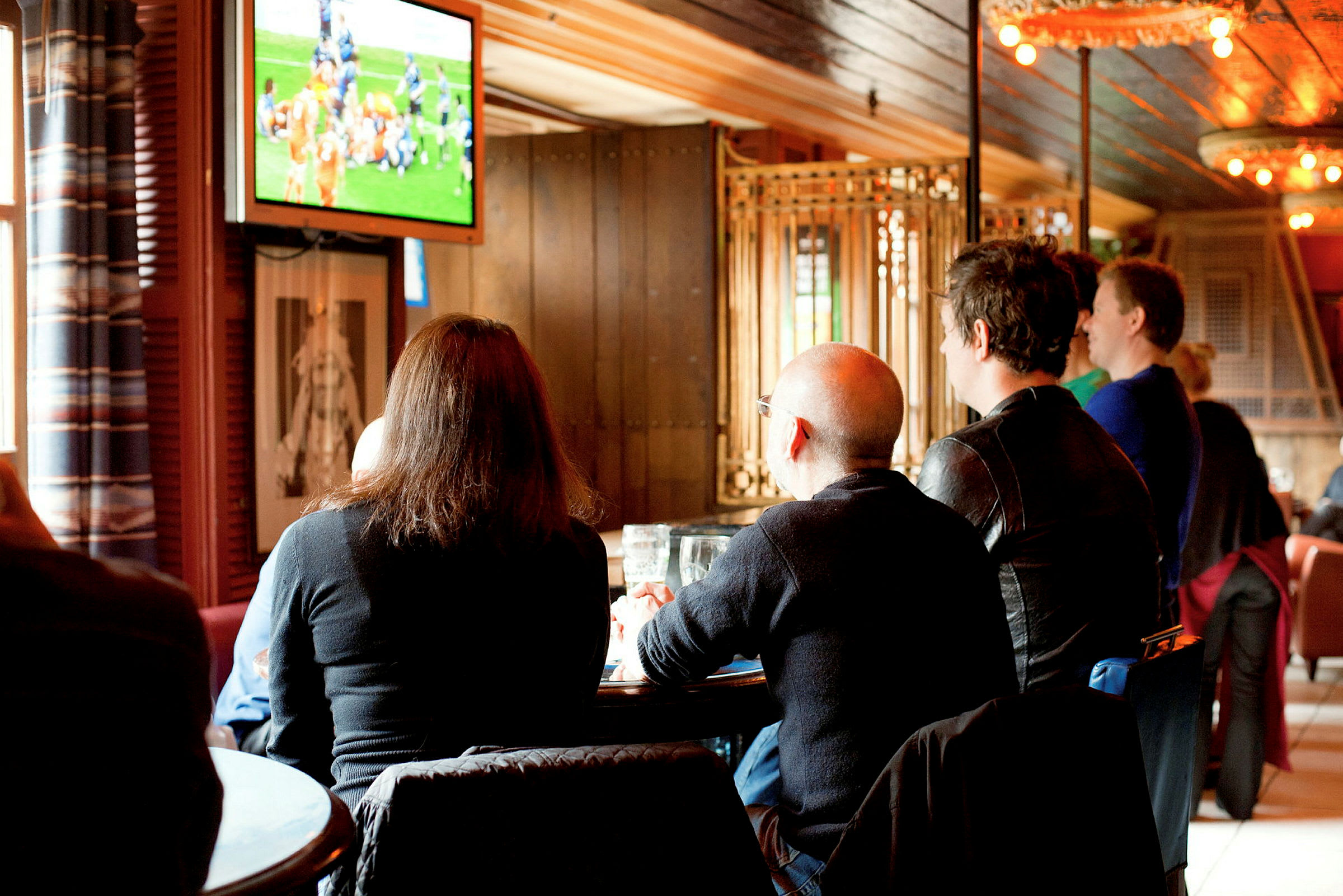 Personer sitter i et lokale og ser på sport på en TV-skjerm. (AI-generert tekst)