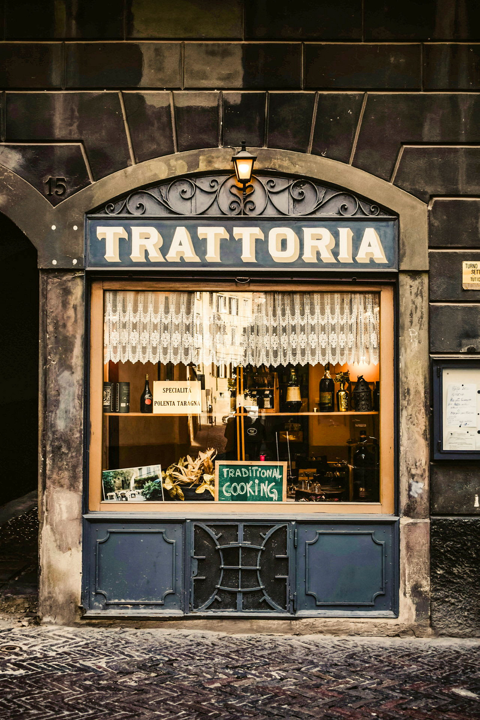 Et butikkvindu til en trattoria med et skilt som sier 'Traditional Cooking' og dekorasjon. (AI-generert tekst)
