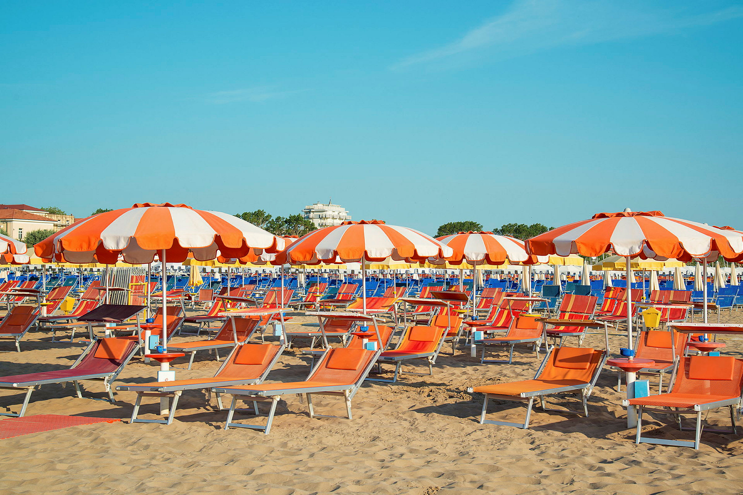 Bilde som viser en sandstrand med oransje og hvite parasoller samt solsenger. (AI-generert tekst)