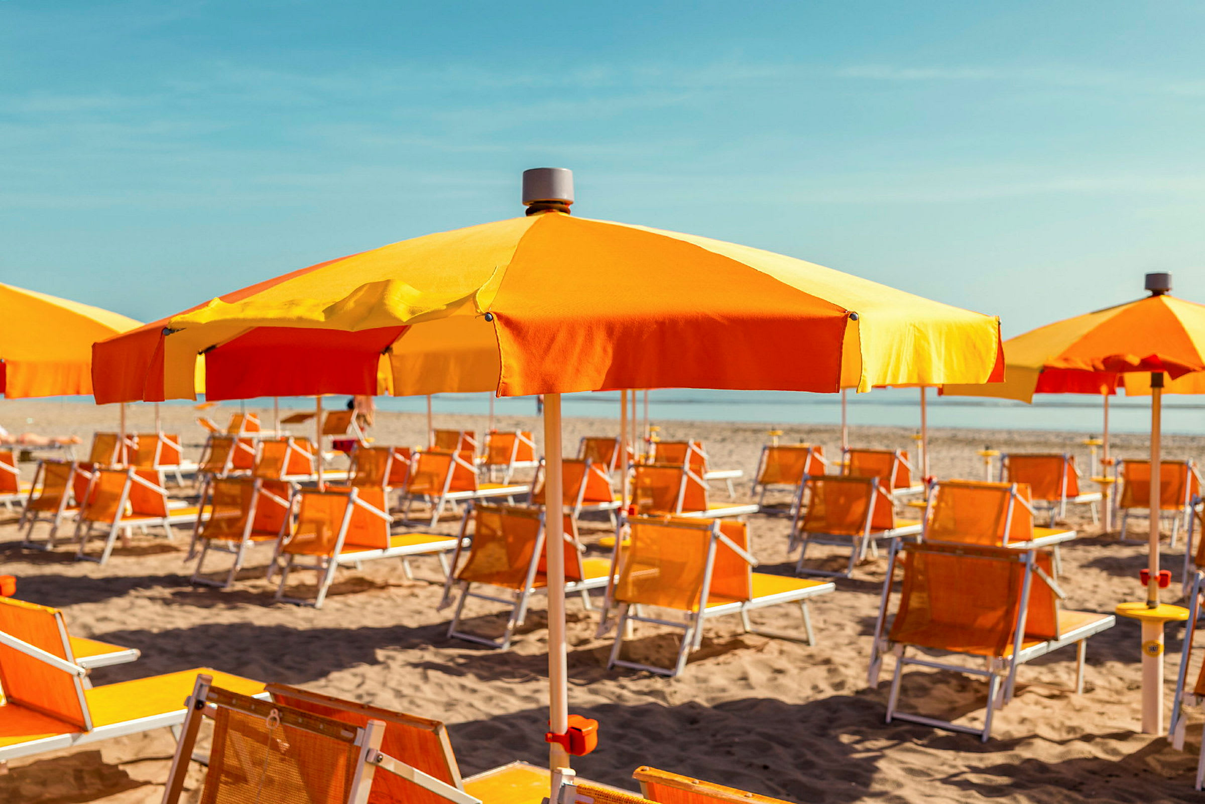 Solstoler og parasoller i oransje og gult står oppstilt på en sandstrand. (AI-generert tekst)