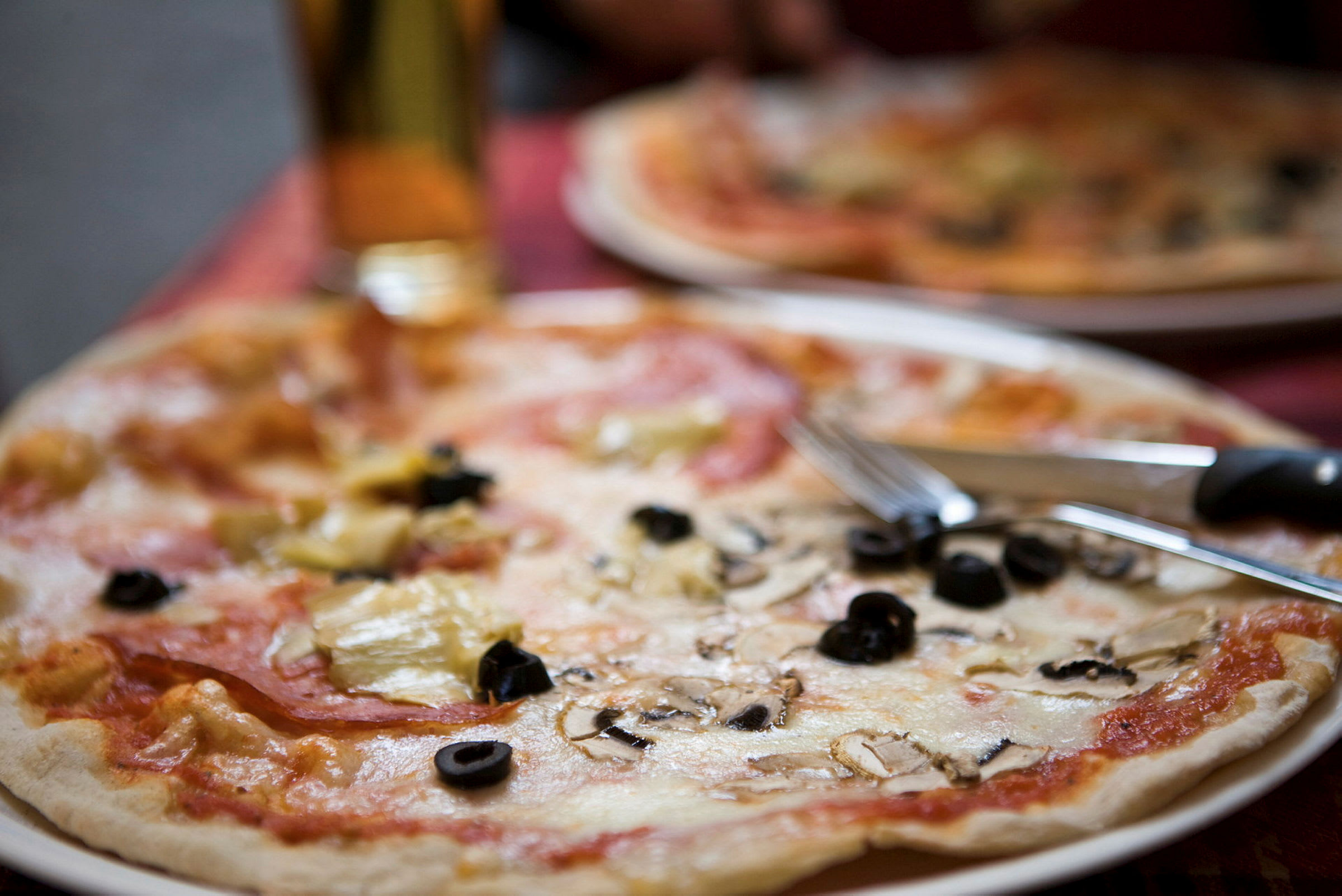 En tallerken med pizza toppet med ost, svarte oliven og sjampinjonger. Bestikk ligger på kanten av tallerkenen. (AI-generert tekst)