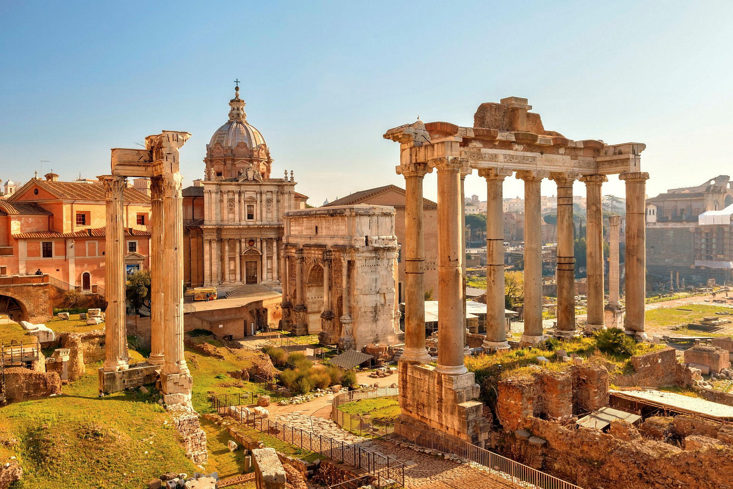 Bildet viser ruiner og bygninger fra antikkens Roma under en klar himmel. (AI-generert tekst)
