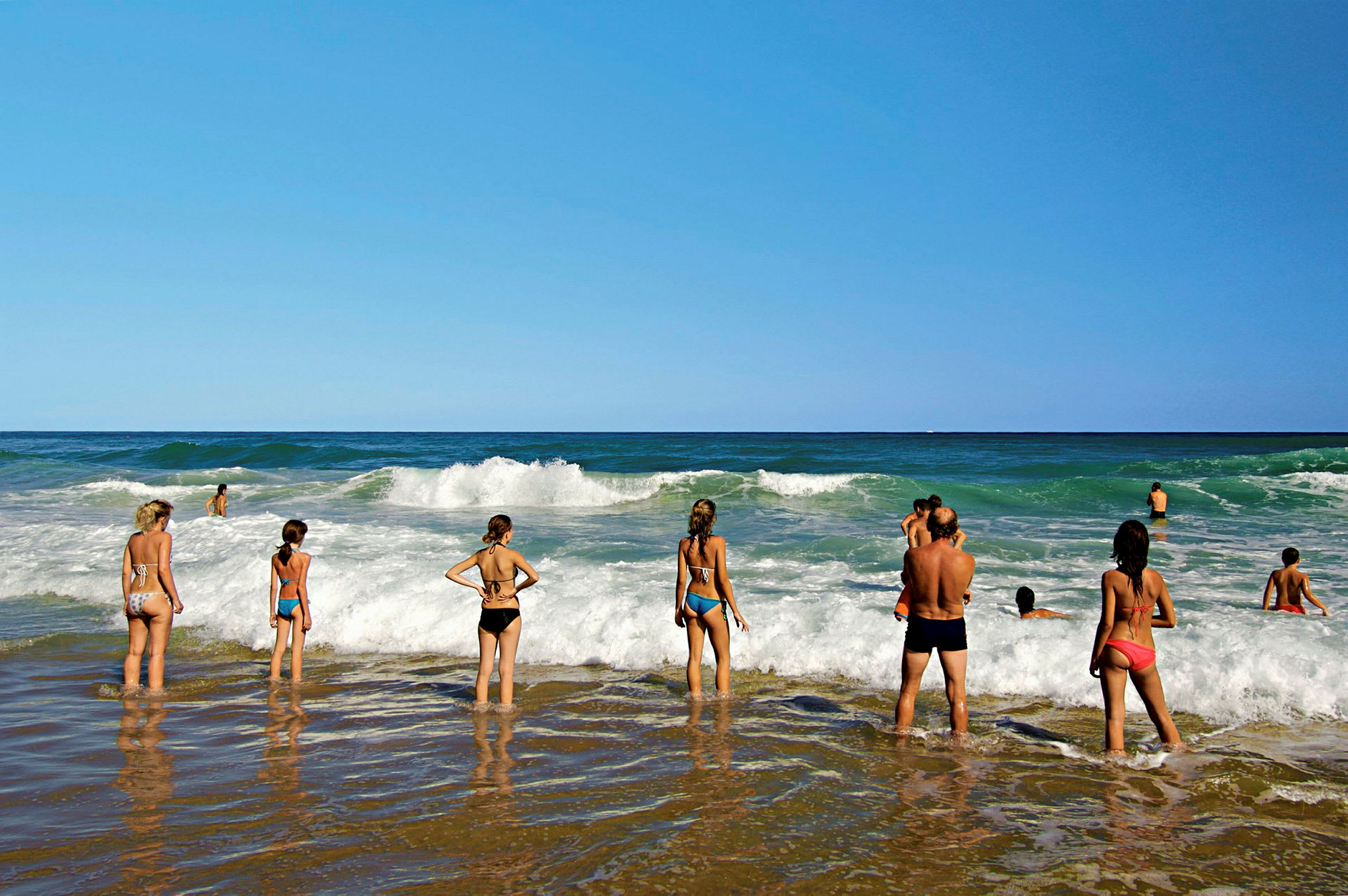 Folk står på en strand og ser ut over bølgene i havet. (AI-generert tekst)