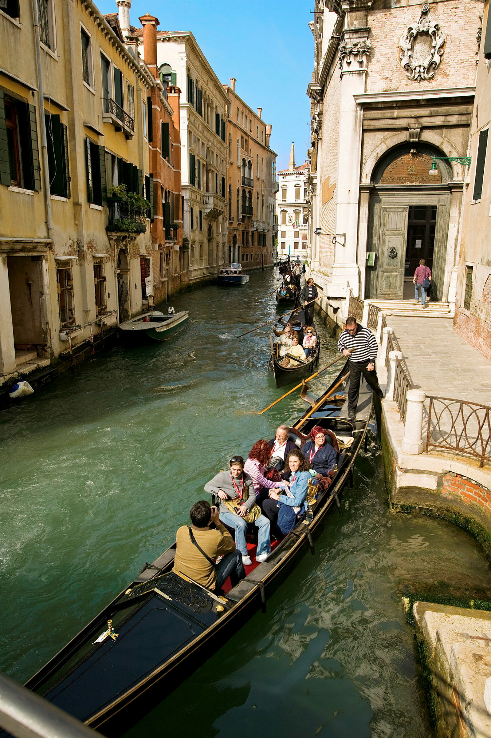En gondol med passasjerer beveger seg langs en kanal i Venezia. (AI-generert tekst)