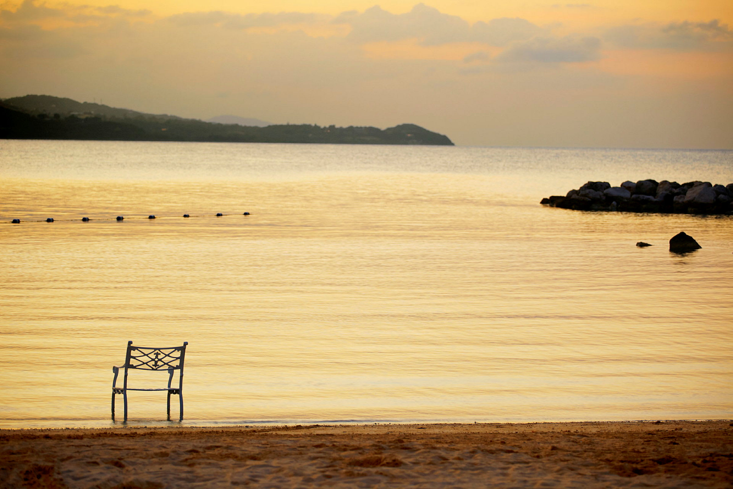 En stol plassert ved stranden med rolig vann og en solnedgang i bakgrunnen. (AI-generert tekst)