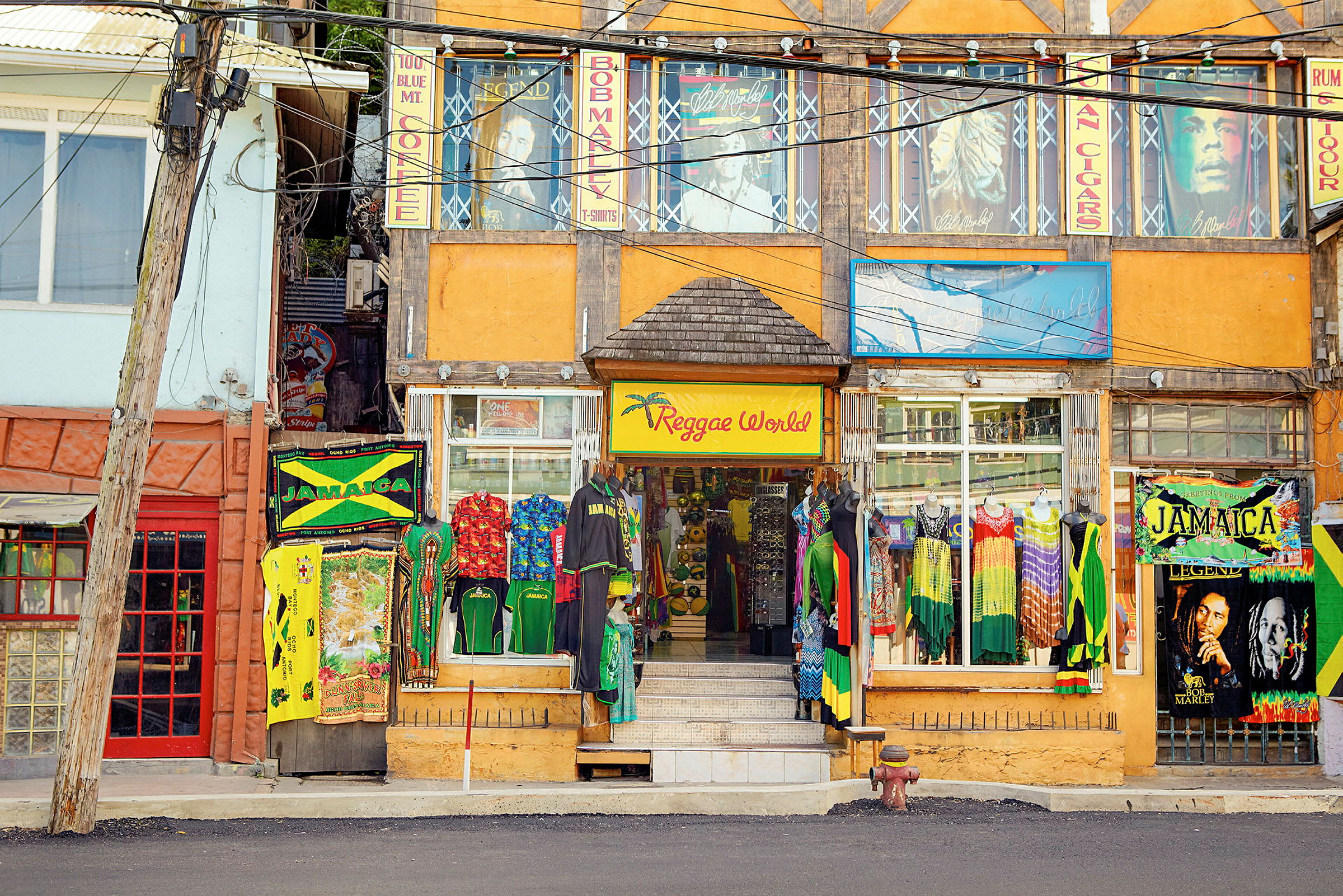 En fargerik butikk med reggae-tema ligger ved en gate, med klær og skilt inspirert av Jamaica. (AI-generert tekst)