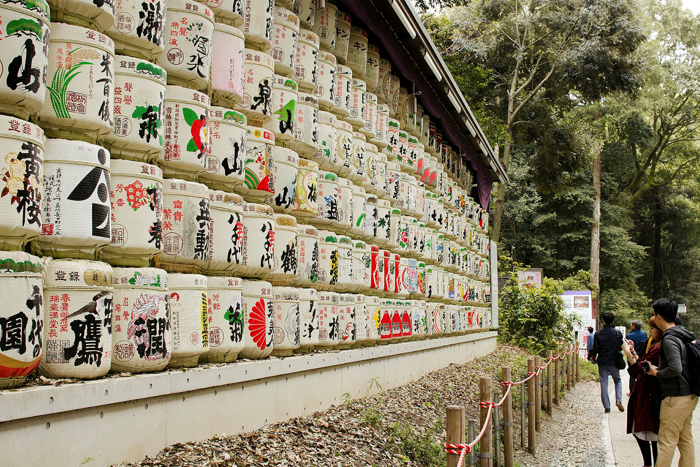 Et bilde med stablede fat dekorert med japanske tegn og motiv, omgitt av en skog. Flere personer ser på fatene. (AI-generert tekst)
