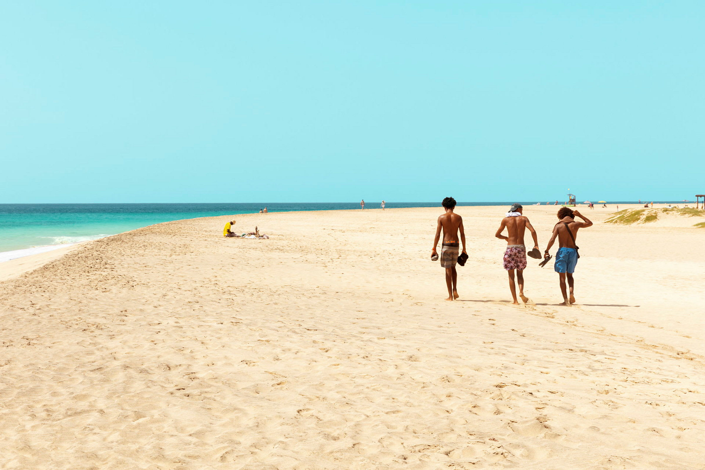 Tre personer går på en sandstrand nær havet. (AI-generert tekst)
