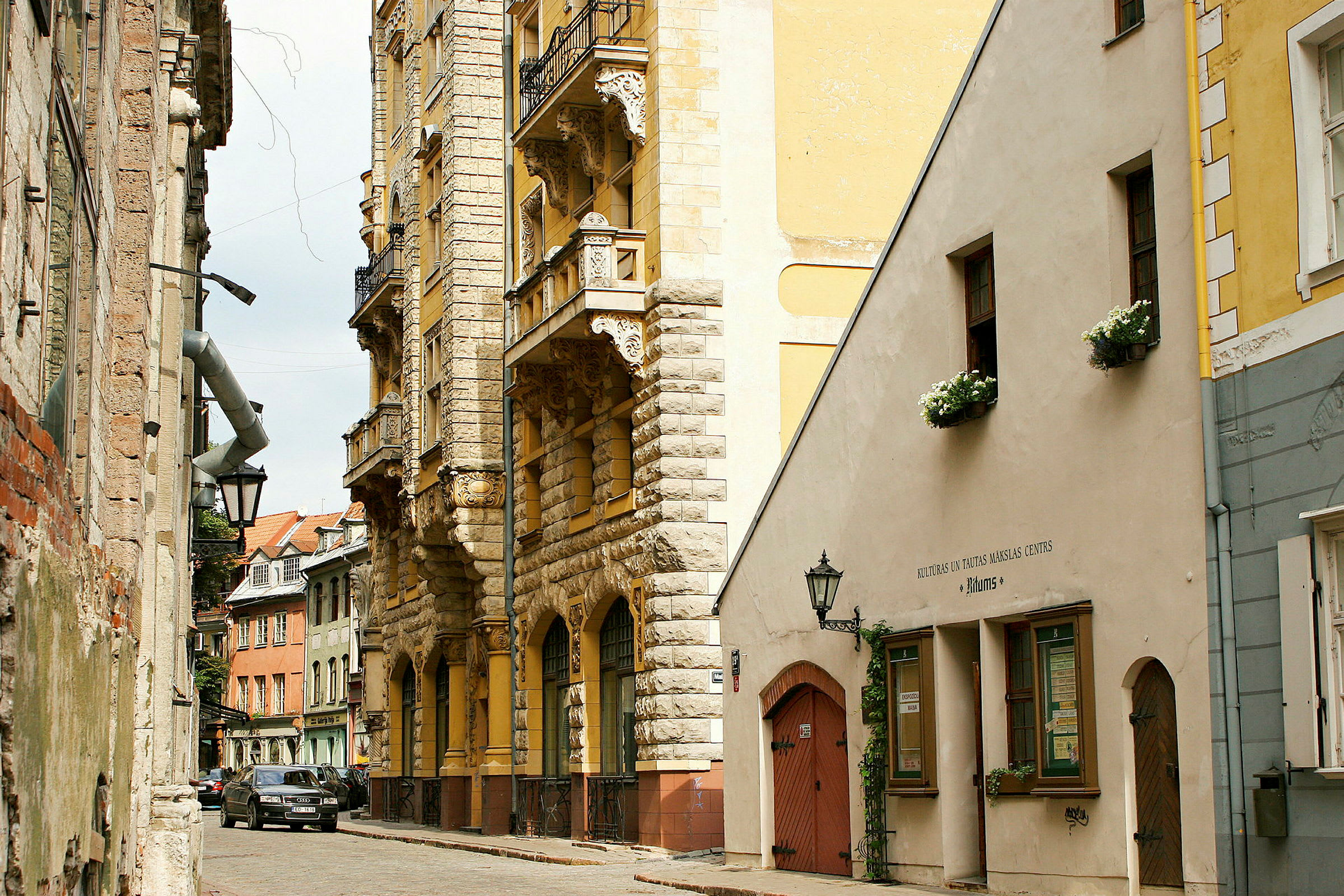 Et smalt gatemotiv med historiske steinbygninger med utsmykkede balkonger og blomsterkasser i vinduene. (AI-generert tekst)
