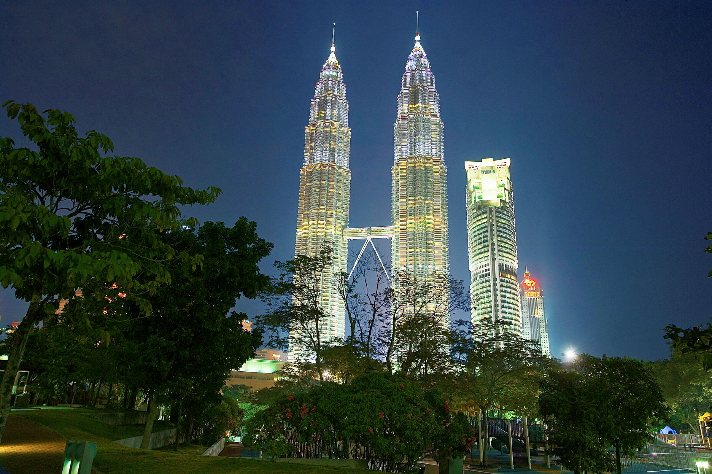 Petronas Twin Towers opplyst om natten med trær i forgrunnen. (AI-generert tekst)