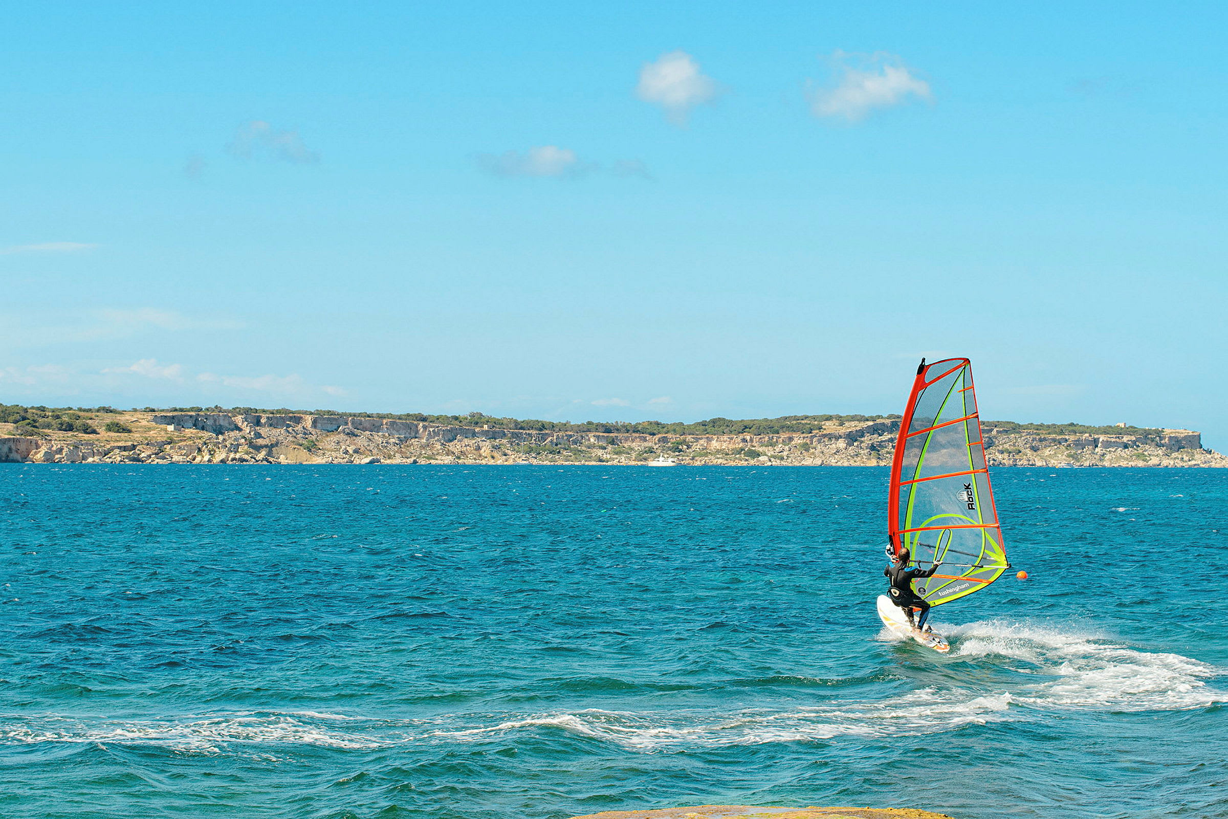 Person som windsurfer på et blått hav med klipper i horisonten. (AI-generert tekst)