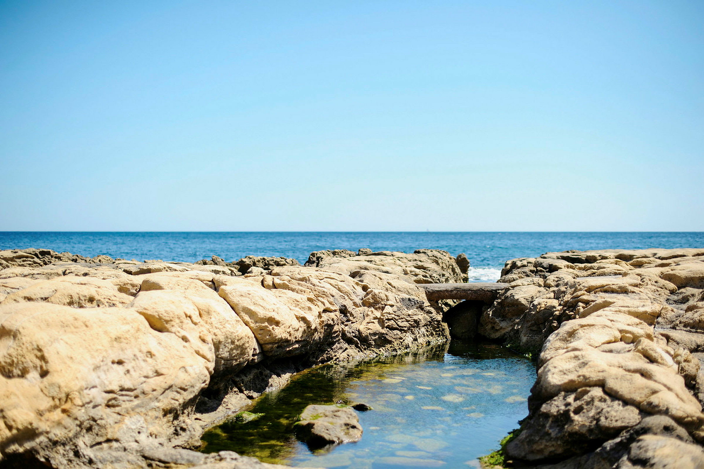 En klippeformasjon med en liten vannpøl og havet i bakgrunnen. (AI-generert tekst)
