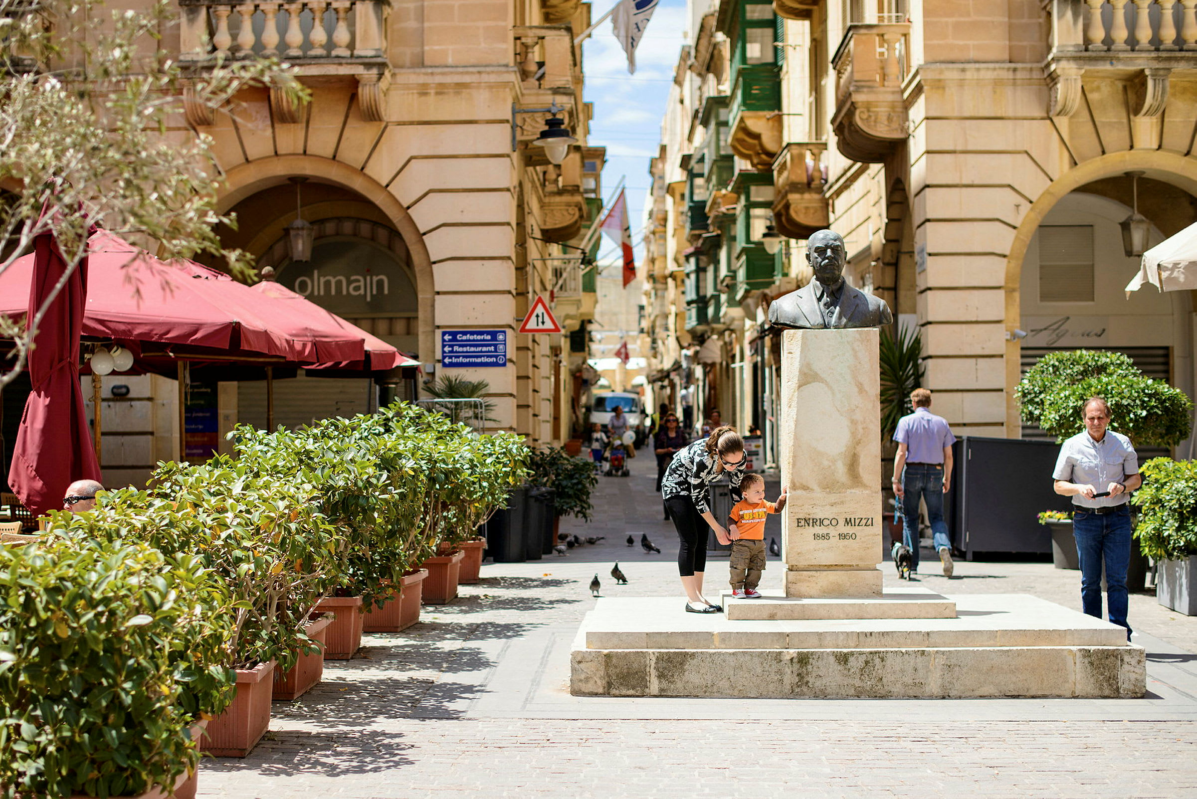 En gate med statuen av Enrico Mizzi, omgitt av bygninger og grøntområder. (AI-generert tekst)