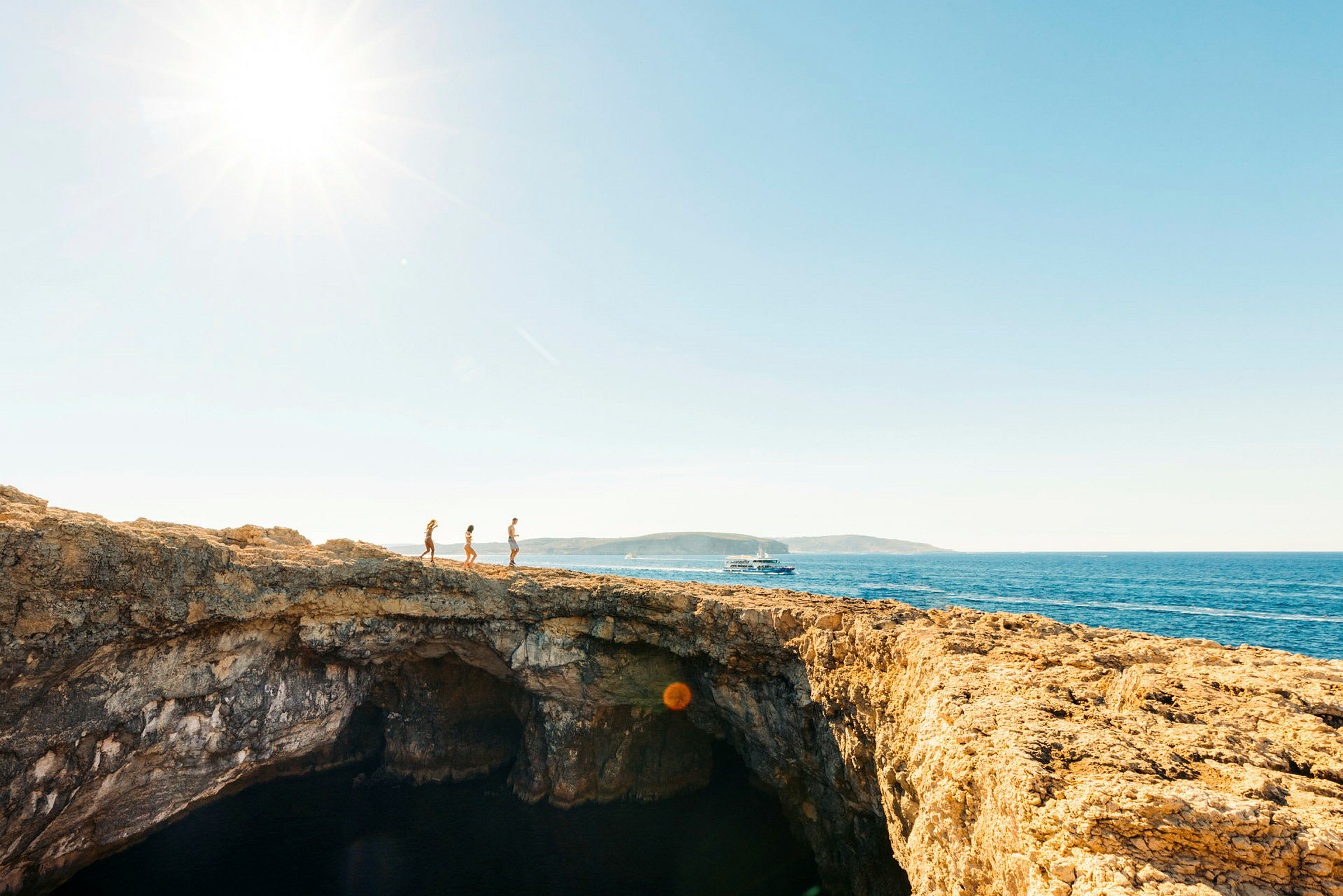 Tre personer går på en klippe med havet i bakgrunnen. (AI-generert tekst)