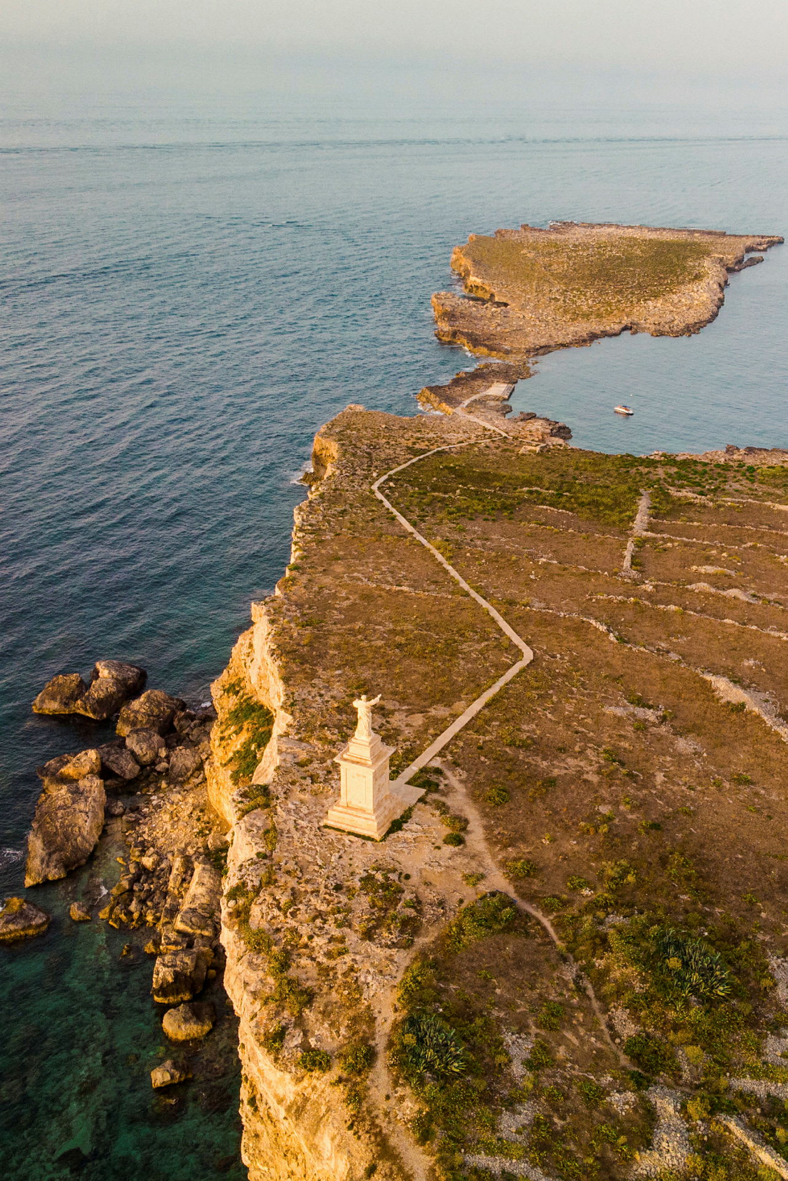 Utsikt over en klippe med en statue nær kanten og havet i bakgrunnen. (AI-generert tekst)