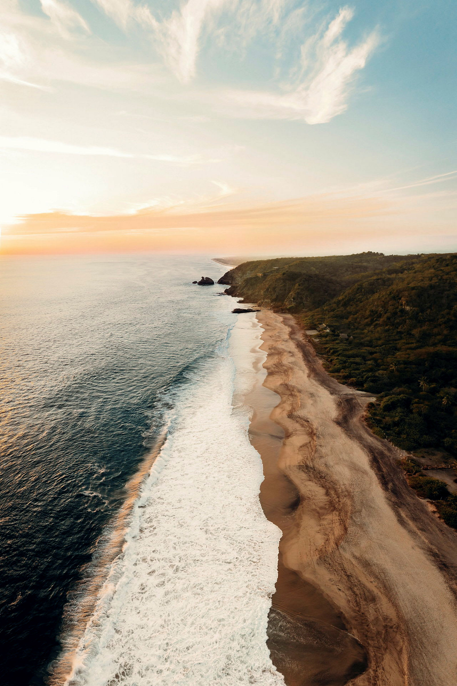 En kystlinje med en bred strand som møter bølgene fra havet under en solnedgang. (AI-generert tekst)