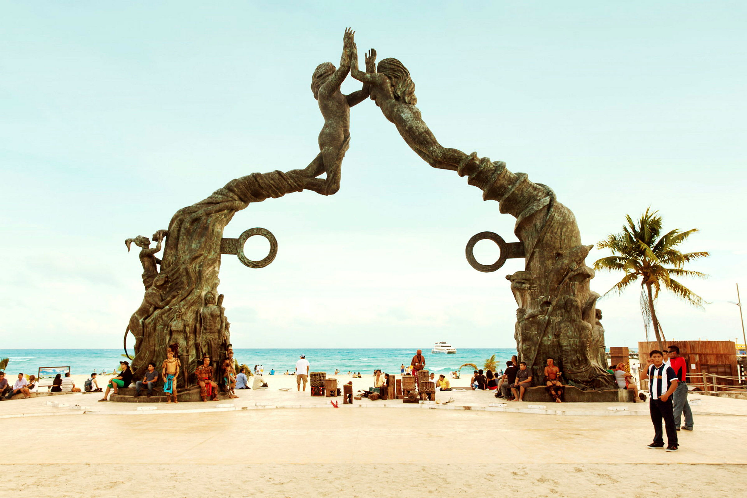 Et monument på stranden med to steinskulpturer som danner en bue. Bak monumentet kan man se havet og mennesker som oppholder seg på stranden. (AI-generert tekst)