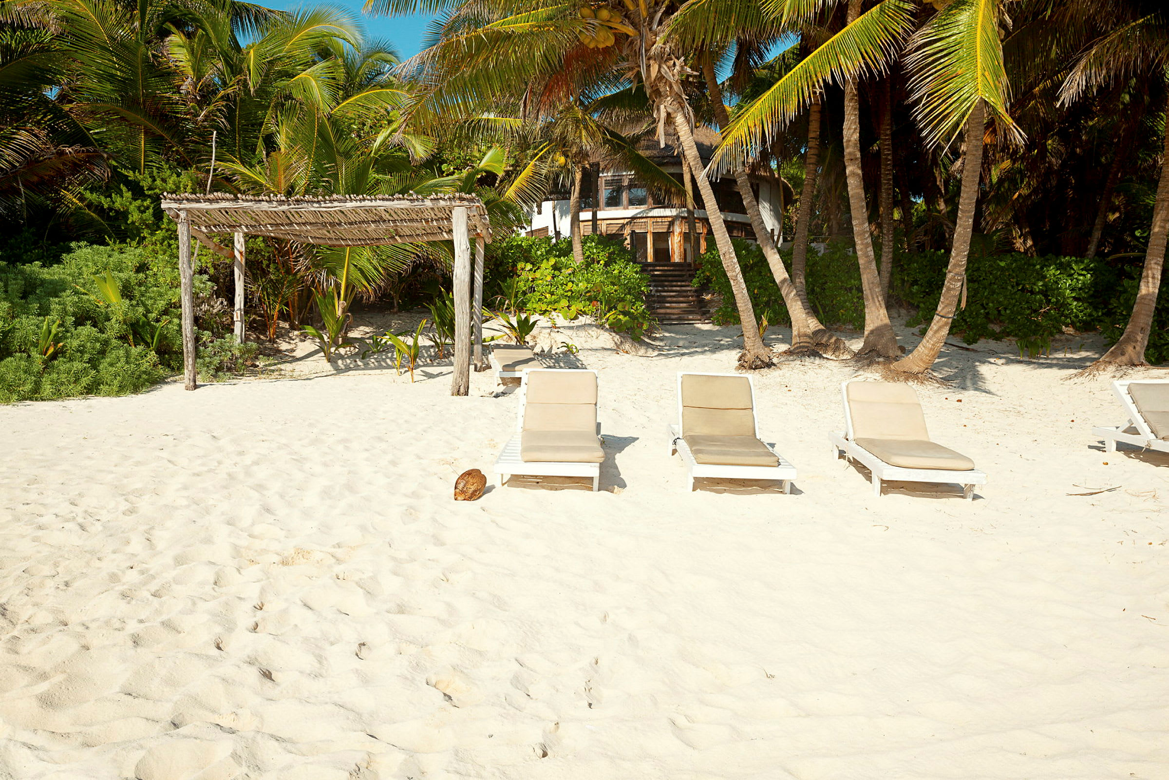 Strand med solsenger på hvit sand ved siden av grønne palmer og vegetasjon. (AI-generert tekst)
