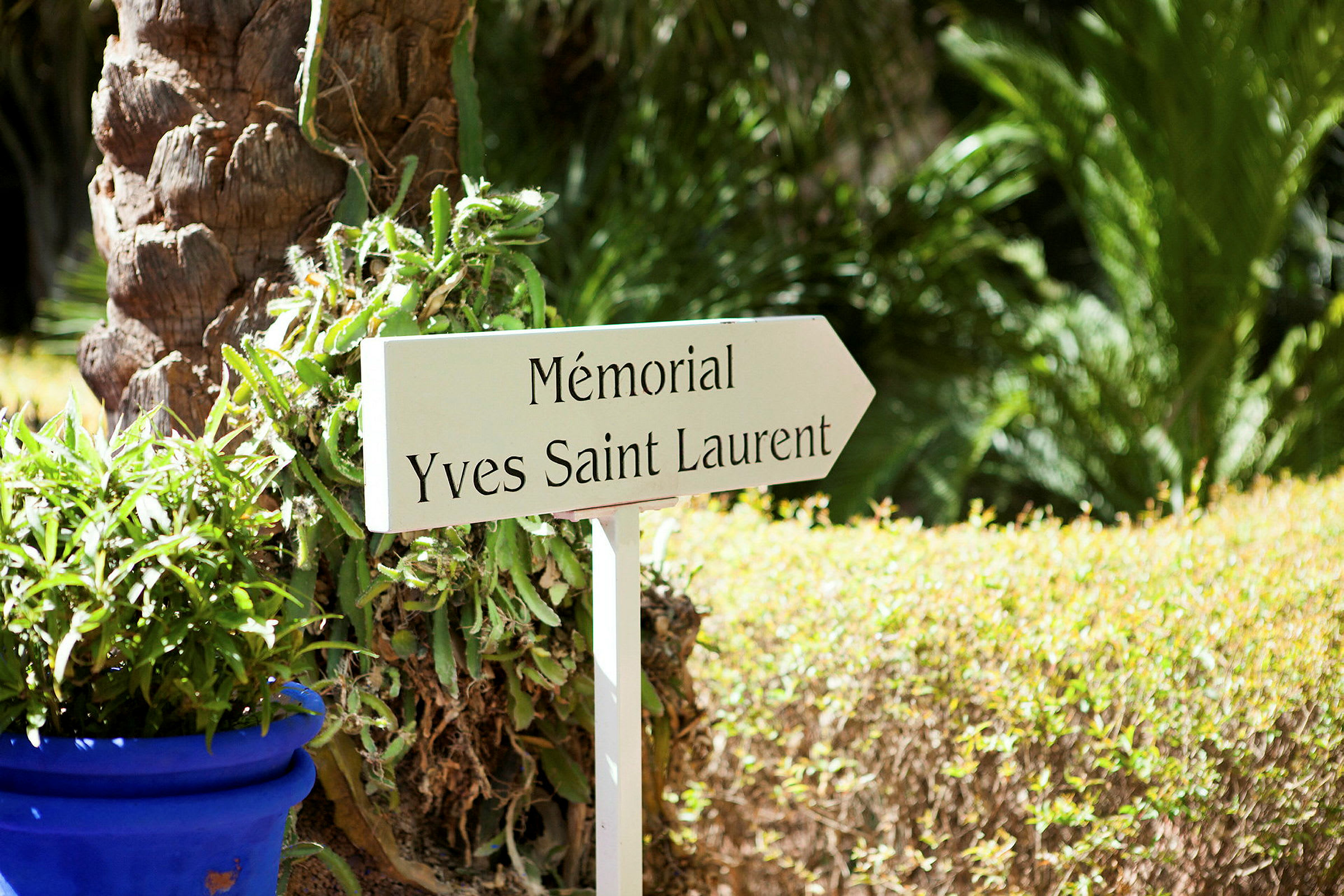 Et skilt merket 'Mémorial Yves Saint Laurent' i en hage med grønt. (AI-generert tekst)