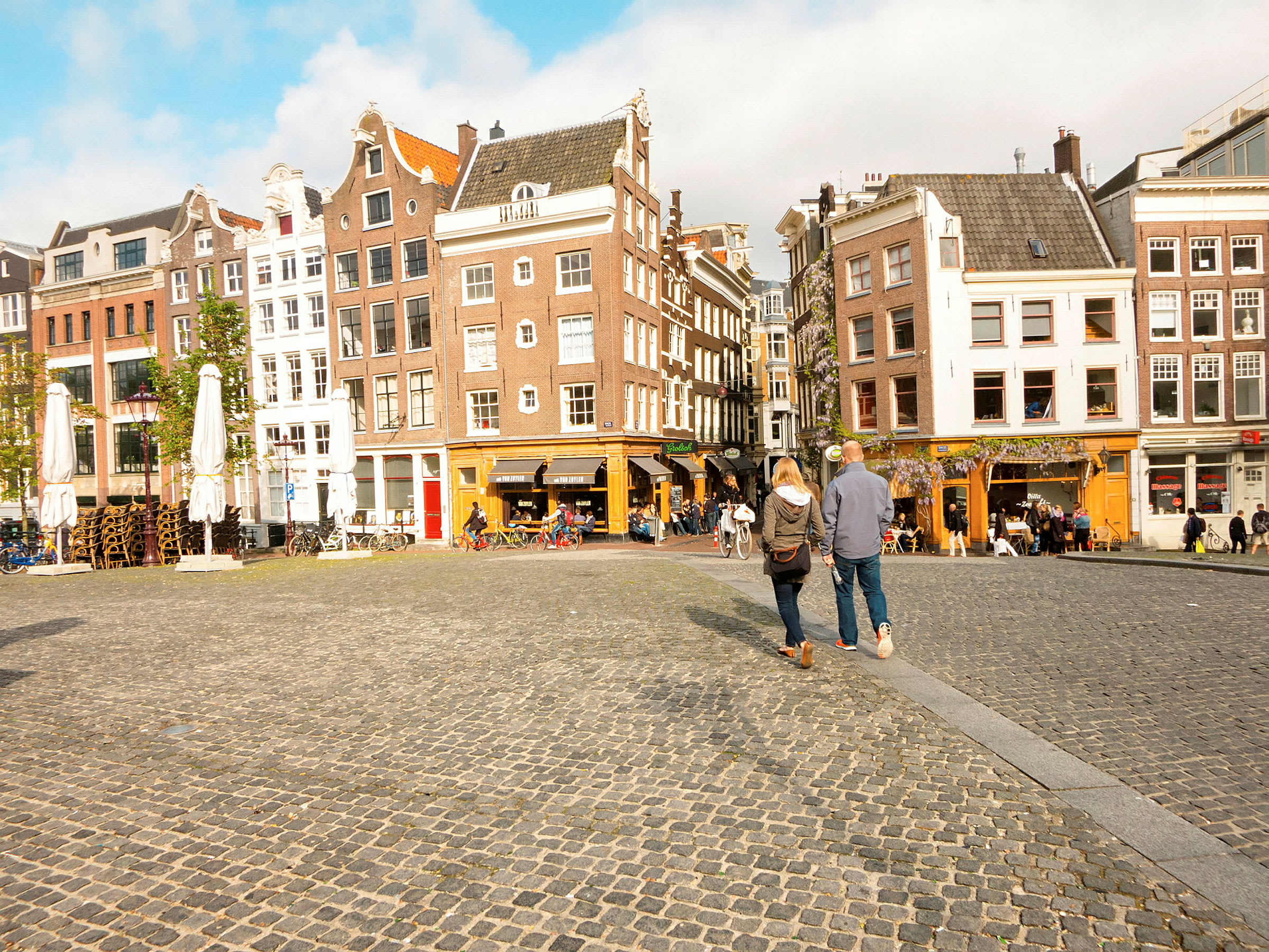 Bilde av et torg med brostein og omkringliggende bygninger i klassisk europeisk stil. To personer går over torget. (AI-generert tekst)