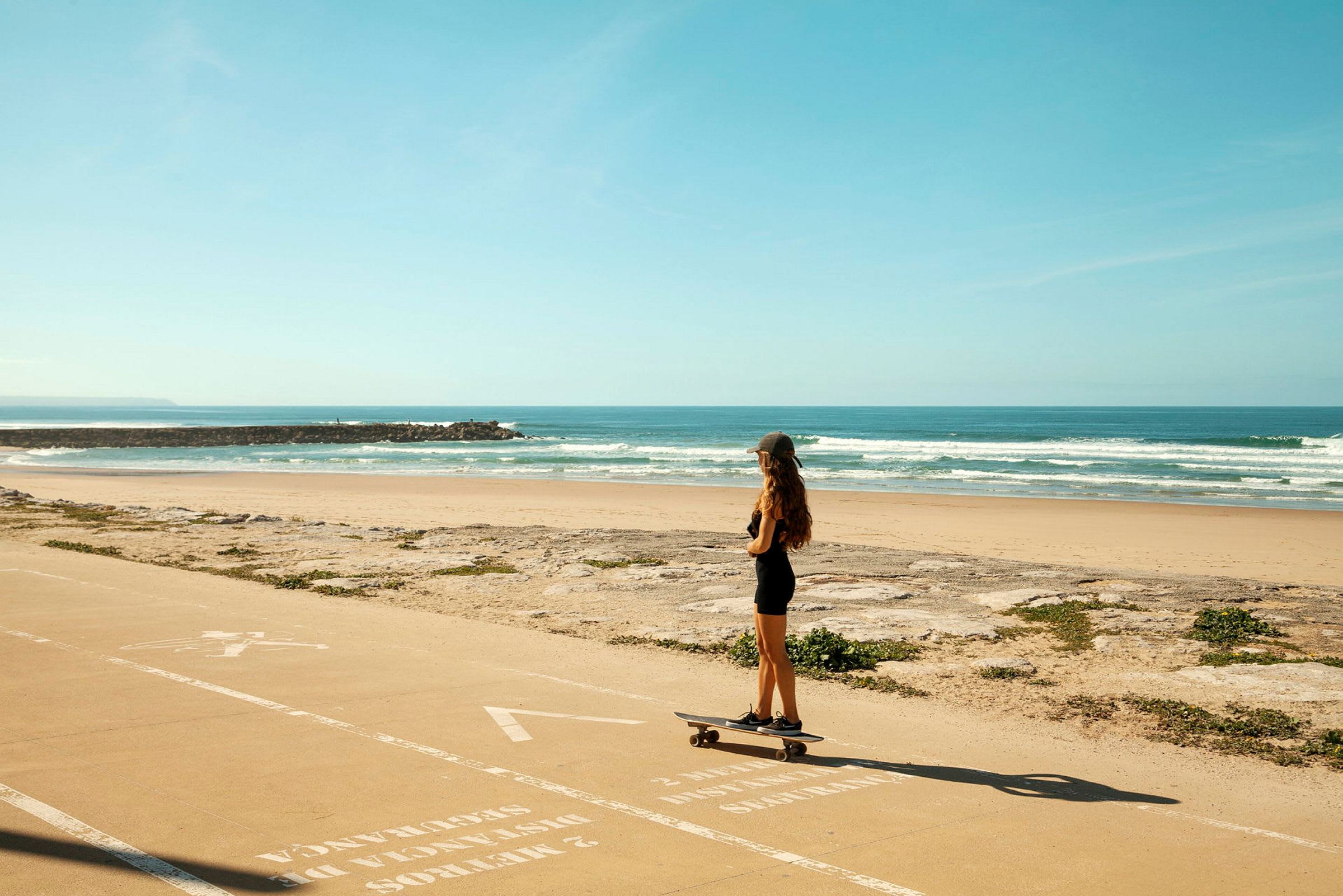 En person står på skateboard på en gangvei ved stranden. (AI-generert tekst)